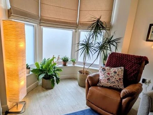 Bright corner with large window, potted plants, and an armchair with a decorative pillow.