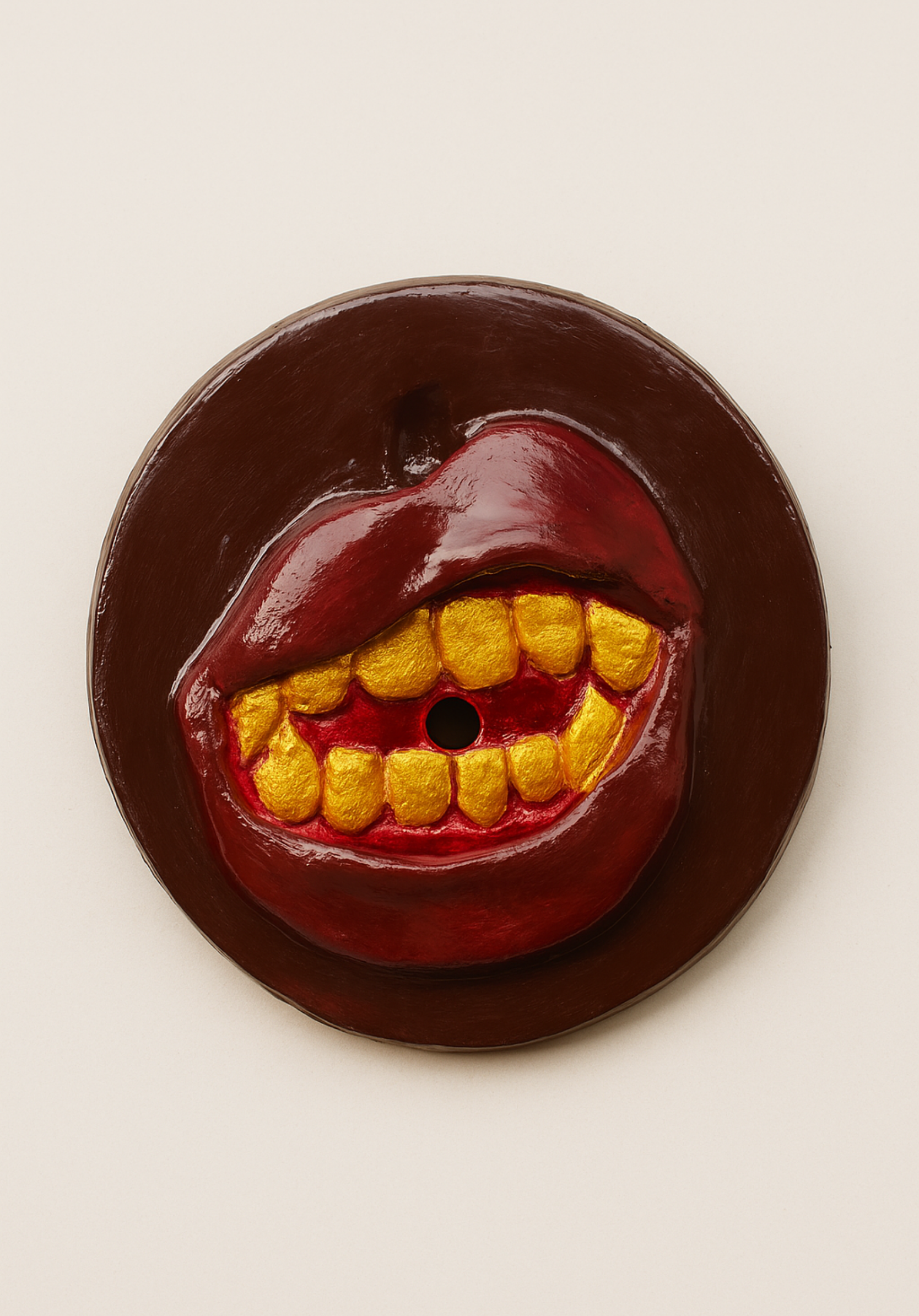 A round, dark brown object with a mouth and teeth design, featuring yellow teeth and red lips, and a black hole in the center.
