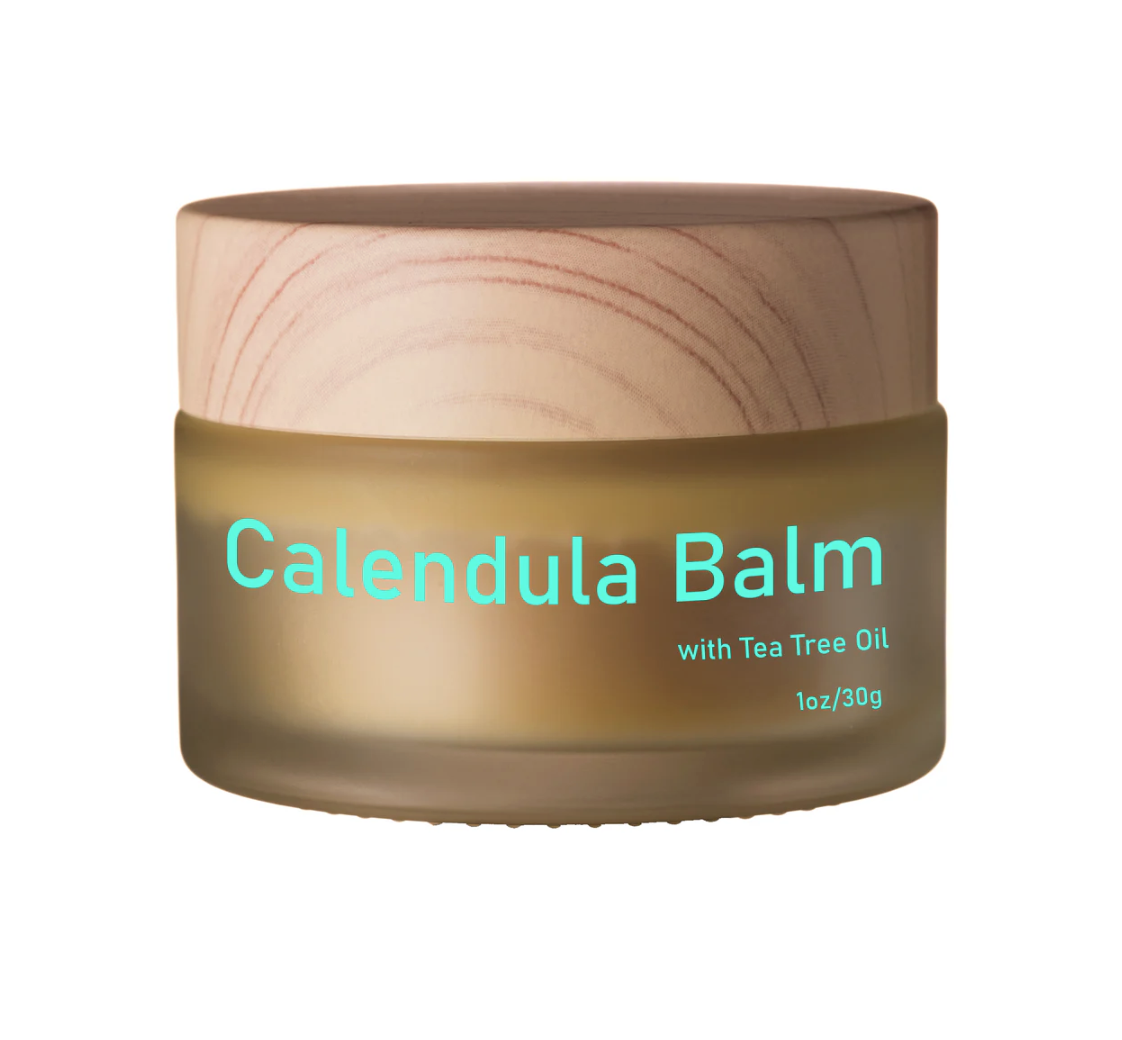 A jar of calendula balm with tea tree oil, featuring a beige lid and label with bright blue text.