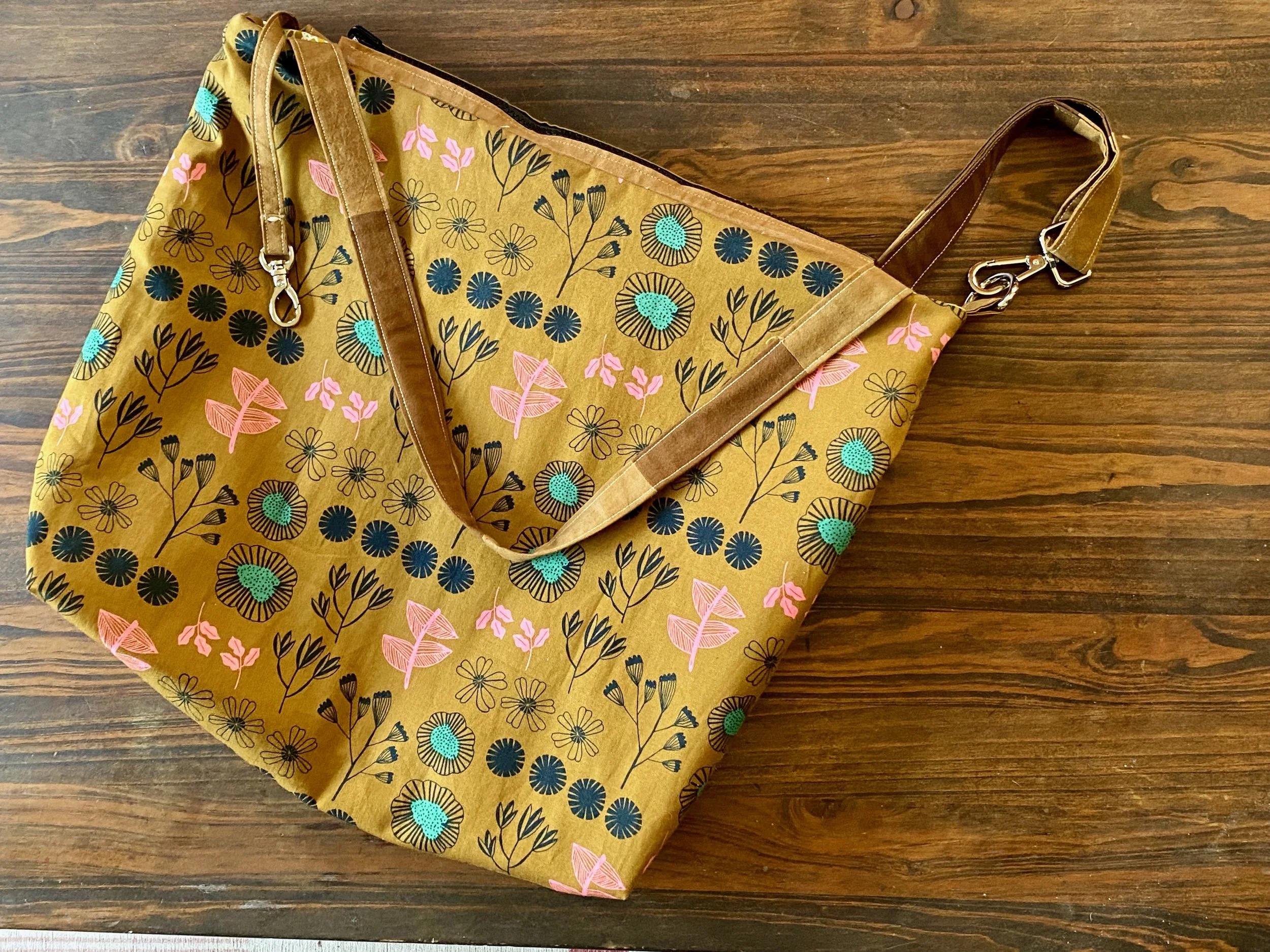 A floral-patterned tote bag with pink, teal, and black flowers on a yellow background, placed on a wooden surface.