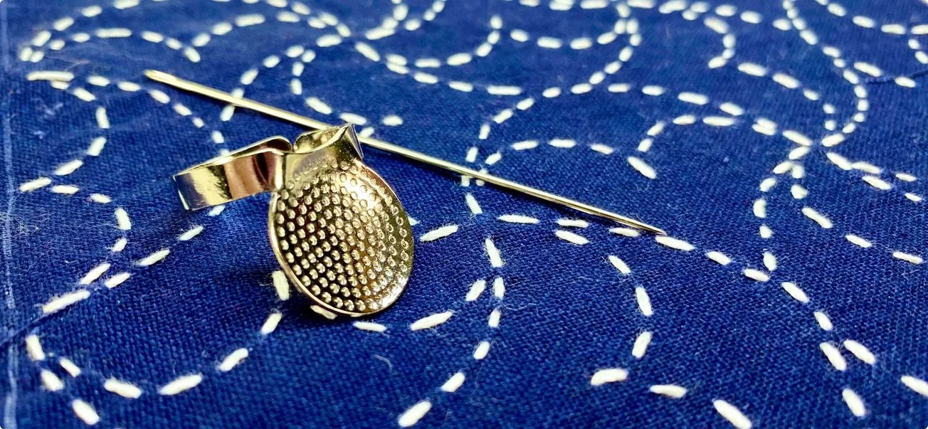 Sashiko needle and palm thimble sashiko tools on blue fabric with flowing white stitches