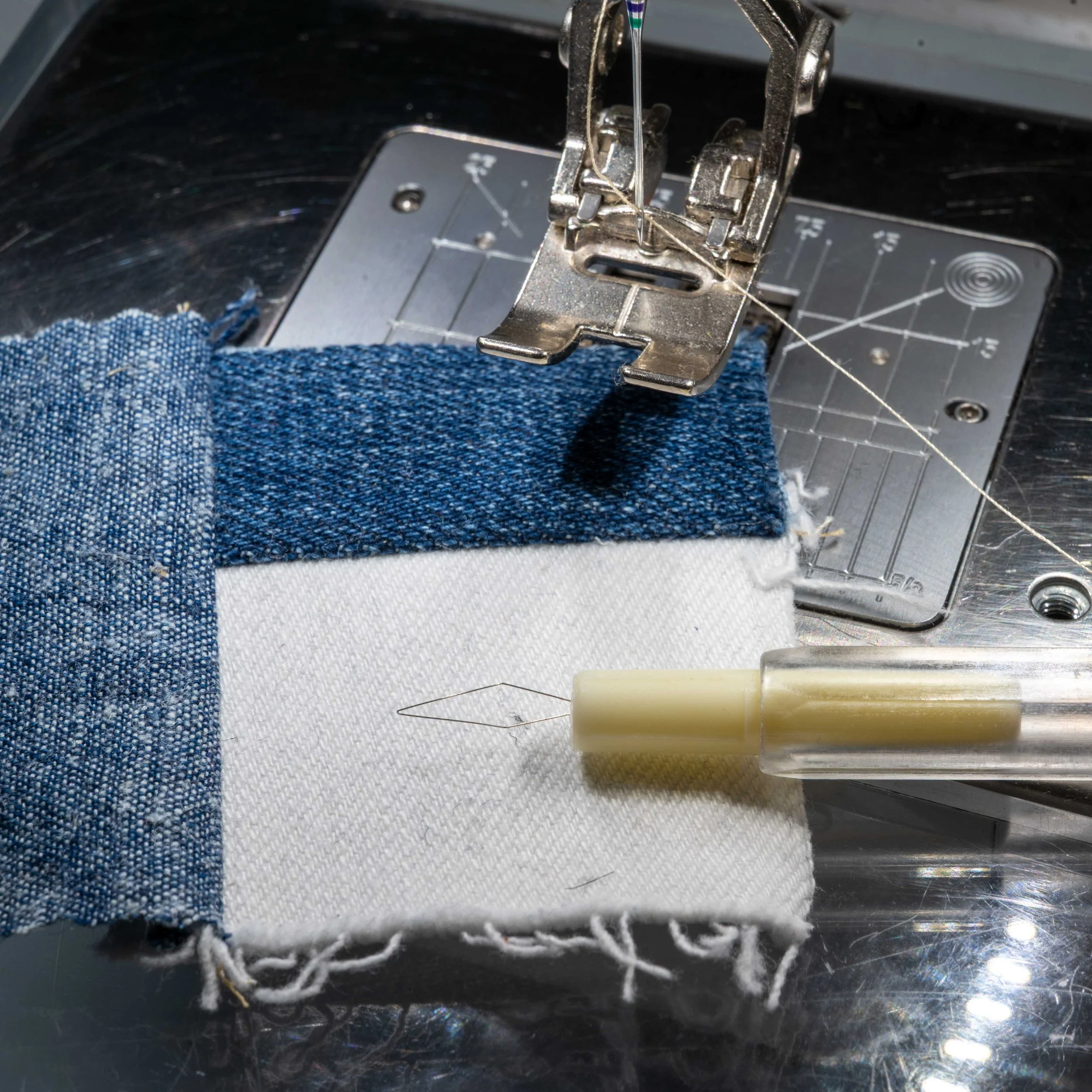 A close-up of a sewing machine needle stitching denim fabric, with the presser foot holding the fabric in place.