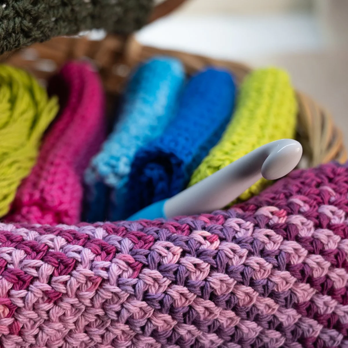 Close-up of a basket filled with colorful rolled yarns, including pink, blue, green, and yellow, with a white lint roller resting among them.
