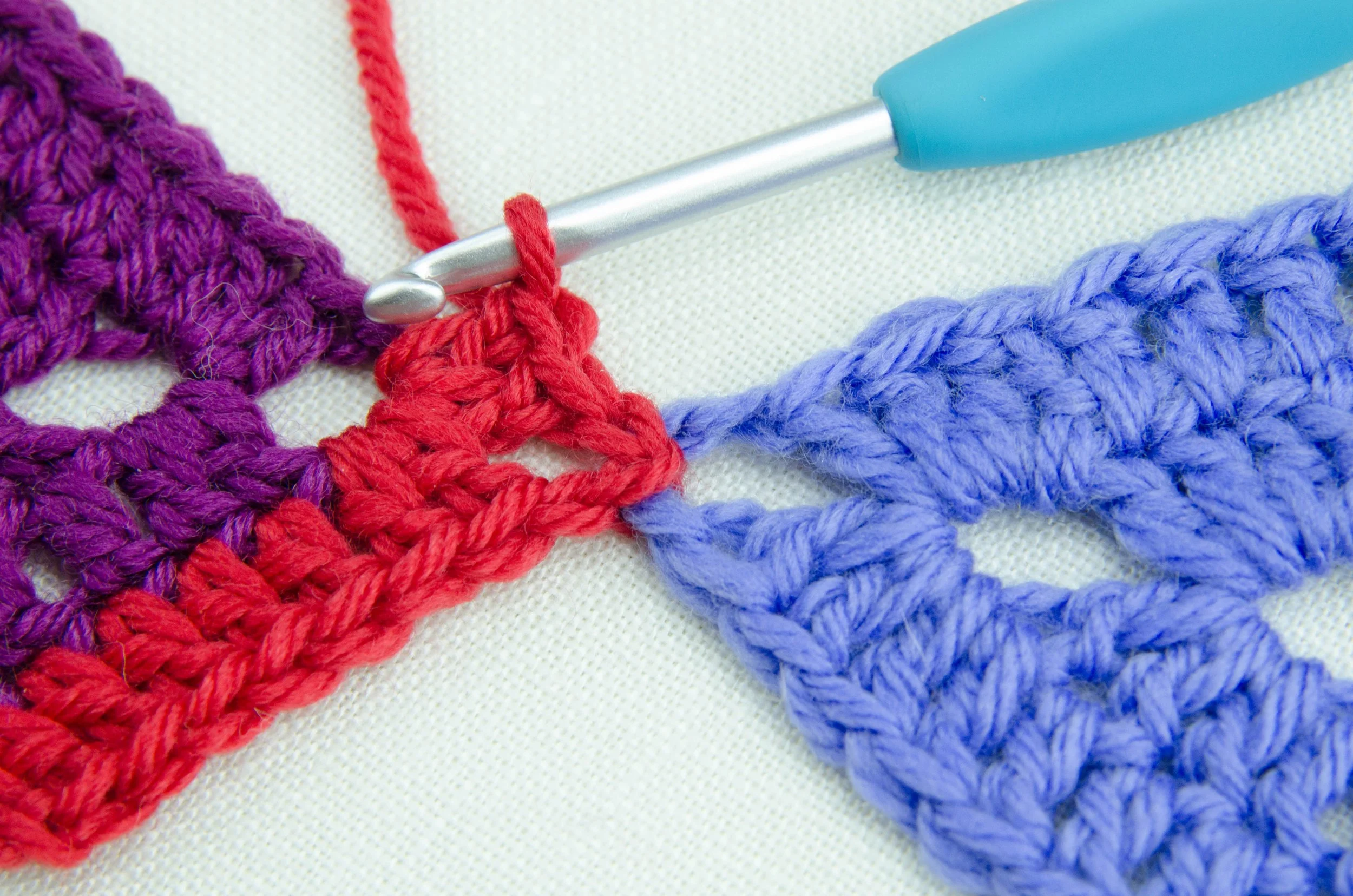 Close-up of colorful crochet project using purple, red, and blue yarn with a crochet hook.