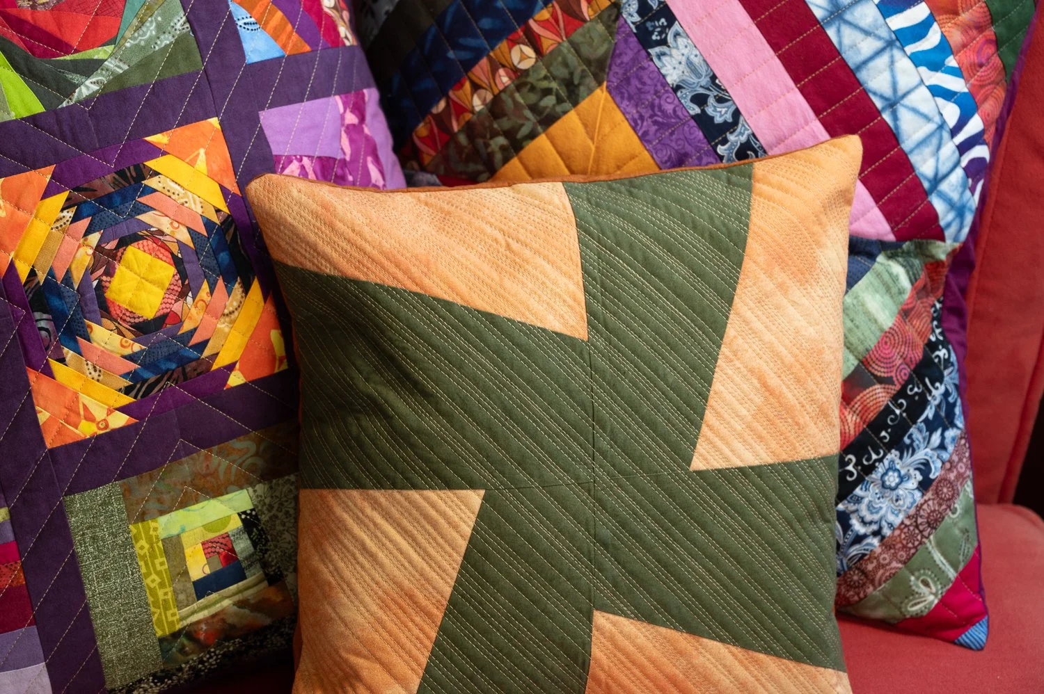 Colorful quilted pillows and blankets with various patchwork patterns and designs on a couch.