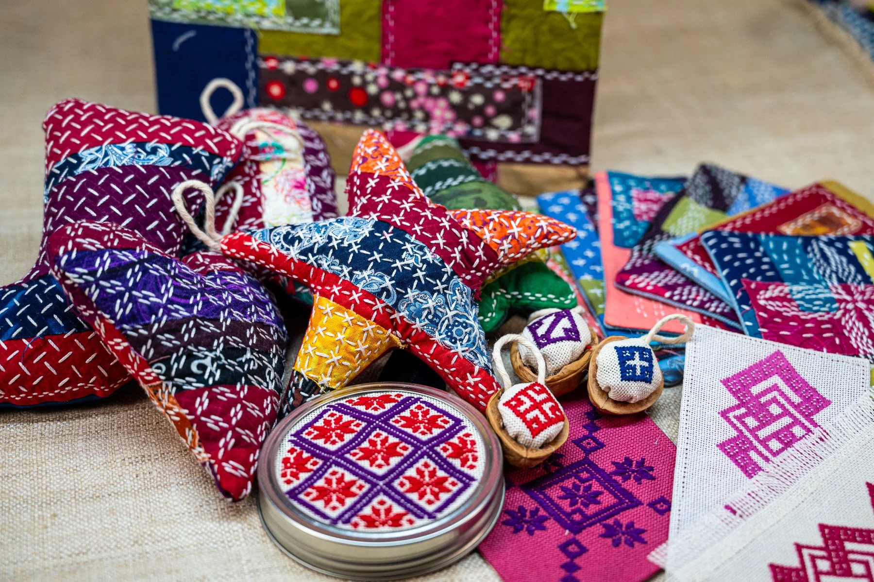 Assorted colorful embroidered fabric ornaments, including stars, hearts, and patches with traditional patterns, displayed on a surface.