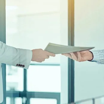 Two people exchanging a document in a modern office setting.