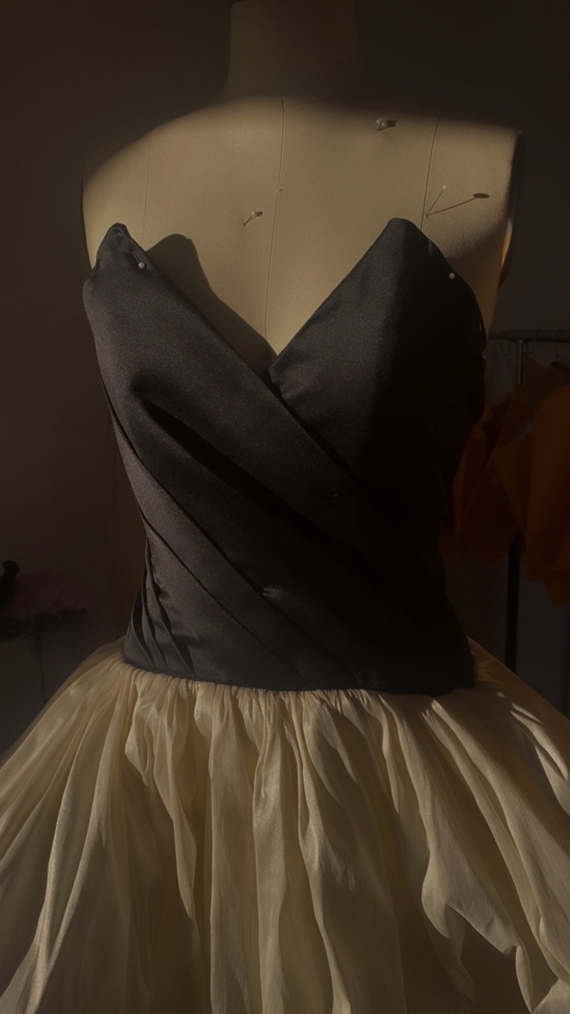 A dress form wearing a strapless black satin top with a sweetheart neckline, and a cream-colored, gathered tulle skirt.