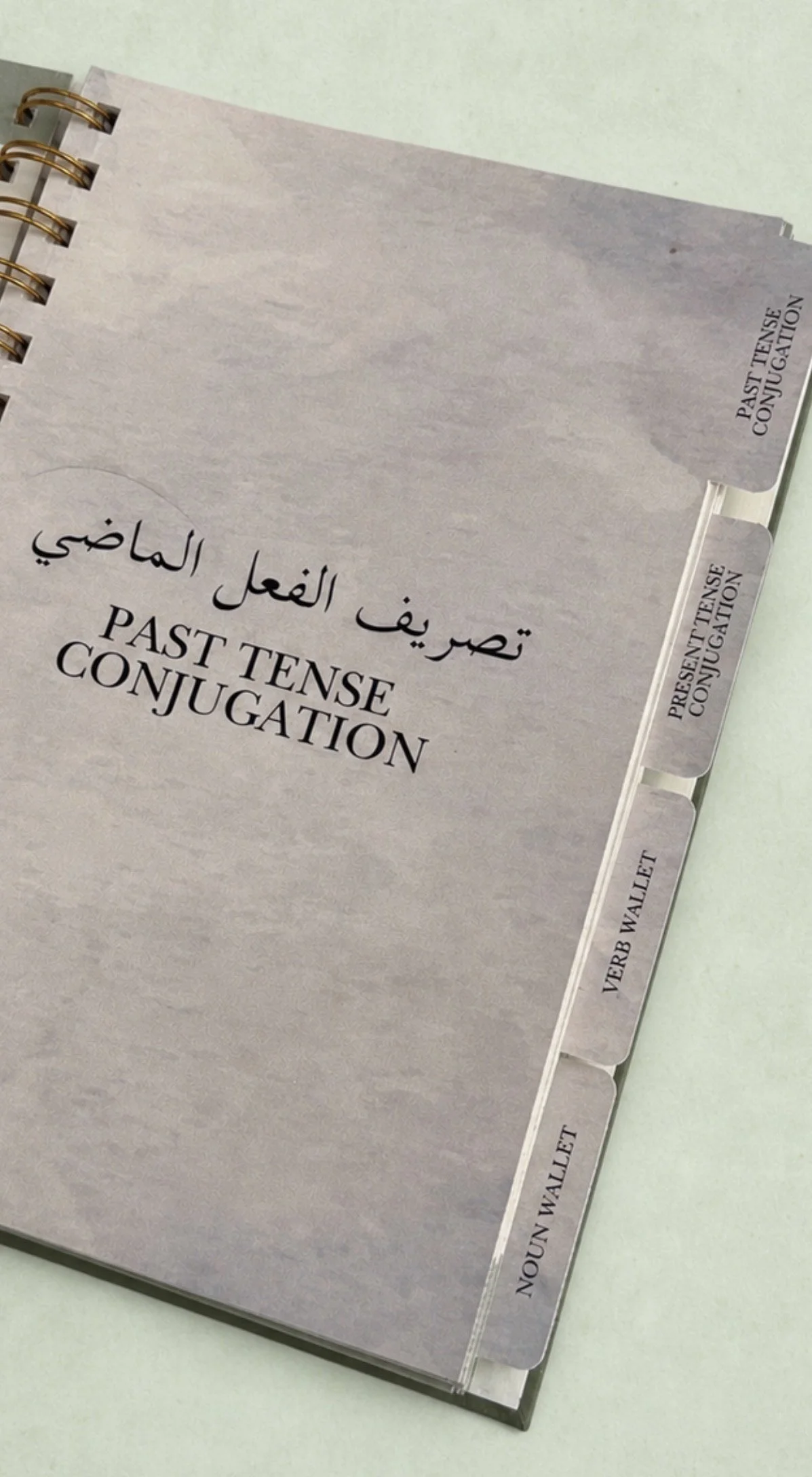 Notebook with a tabbed divider labeled 'Past Tense Conjugation' in Arabic and English.