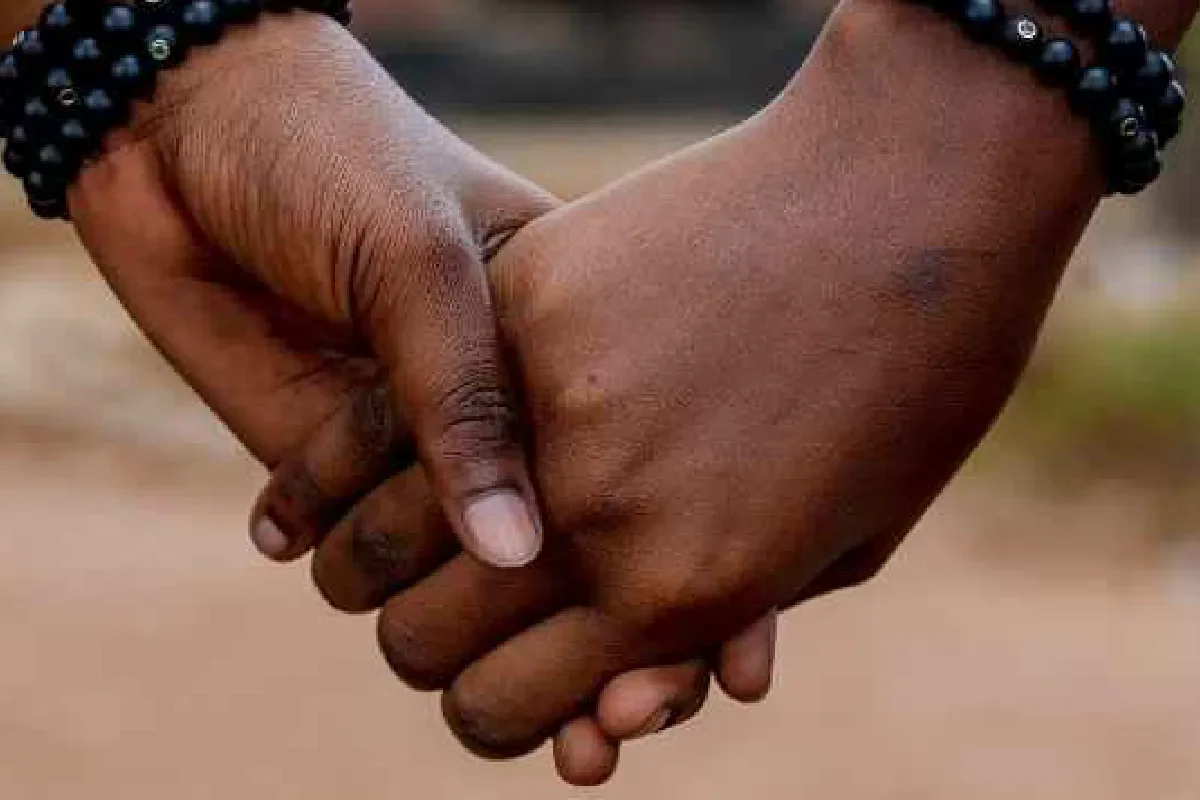 Two people holding hands, one with darker skin and the other with lighter skin, wearing beaded bracelets.