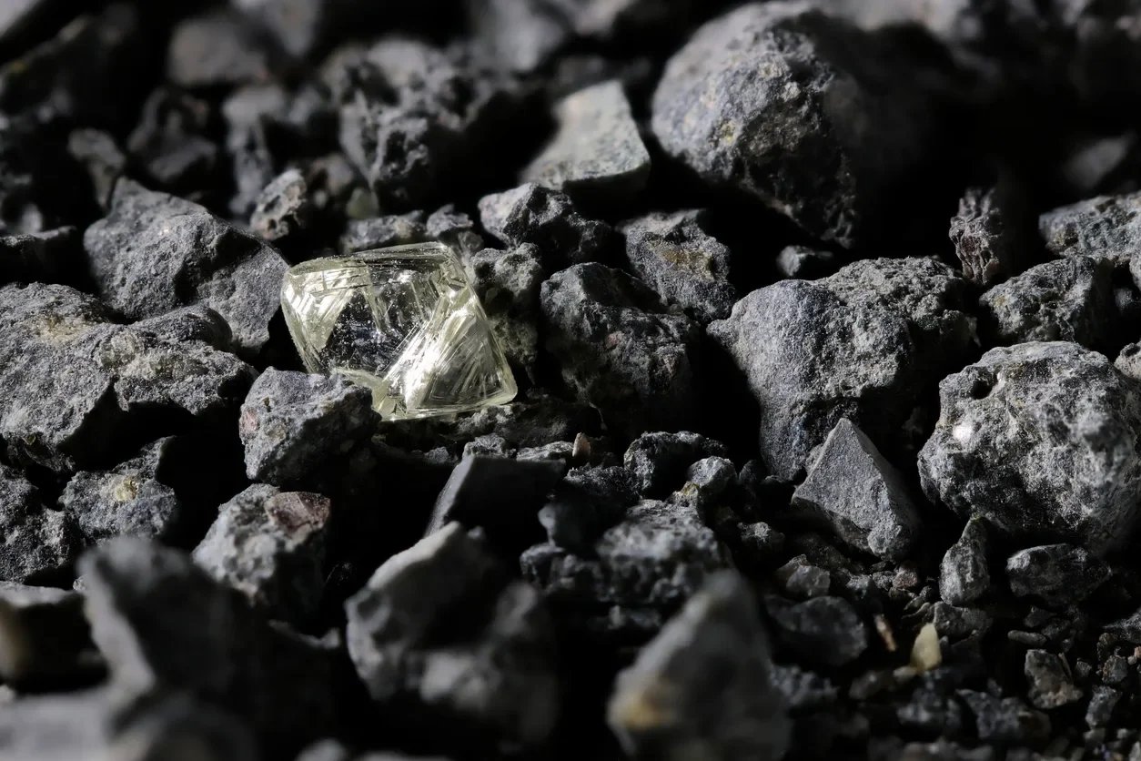 A clear, faceted gemstone or mineral on dark, rough gravel or small rocks.