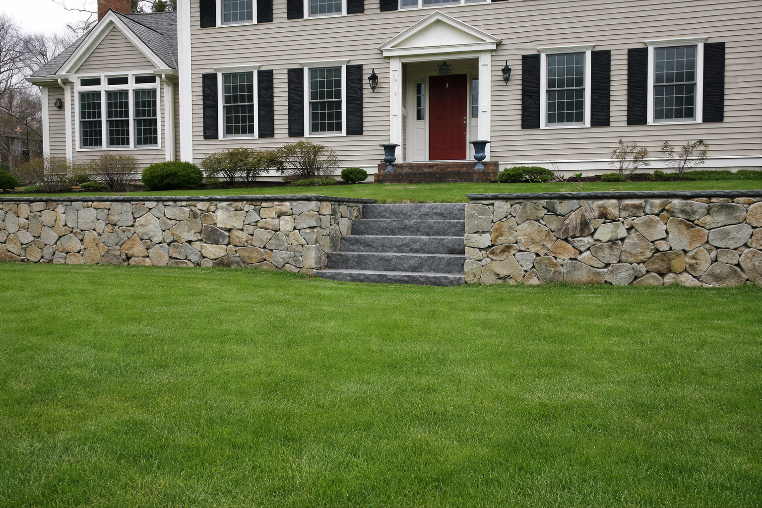 Front view of a house with a stone retaining wall, steps leading to the porch, and a grassy lawn.