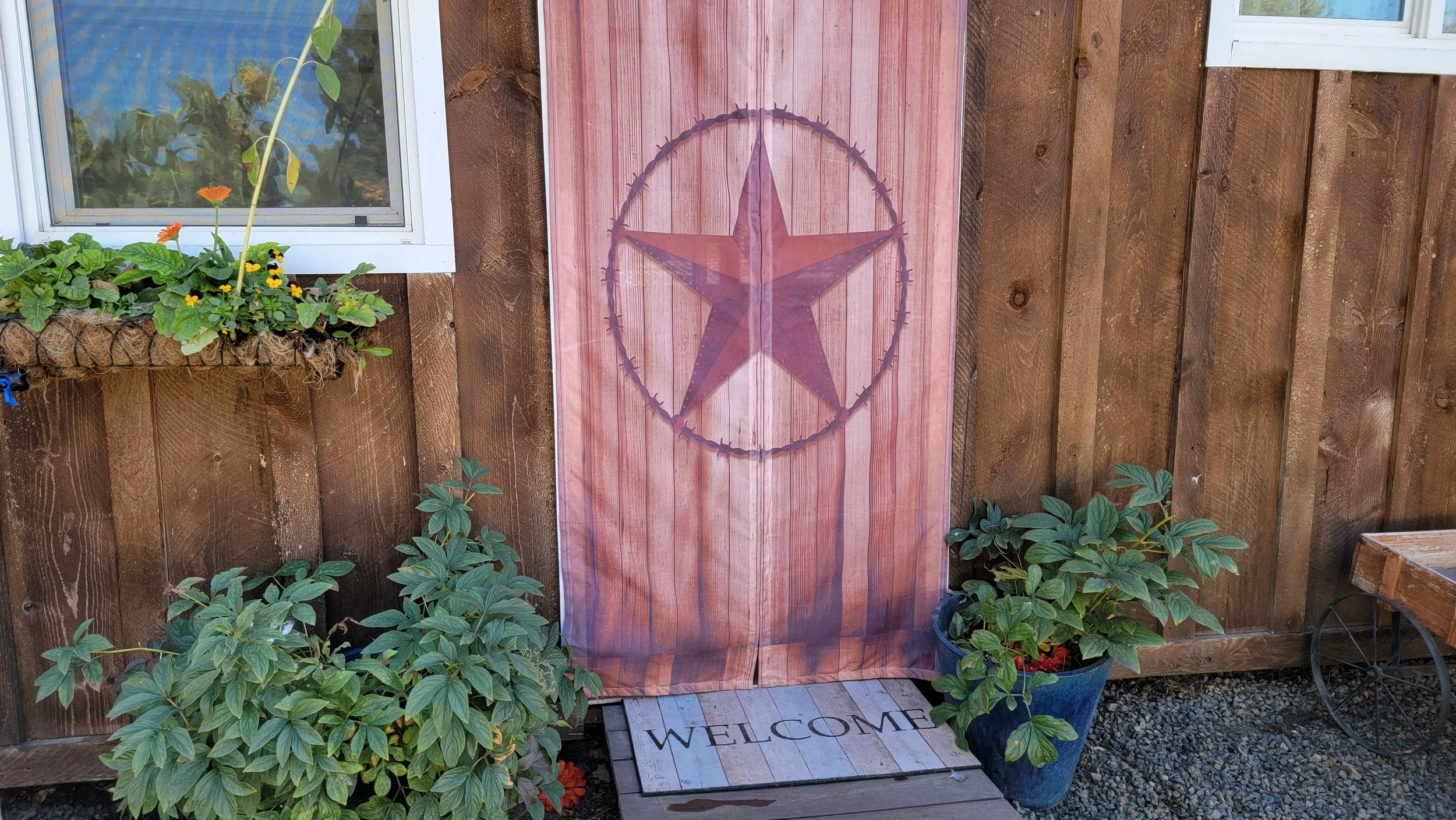 Decorative outdoor space with a wooden fence, potted plants, a 'Welcome' mat, and a fabric covering with a star and circle design.