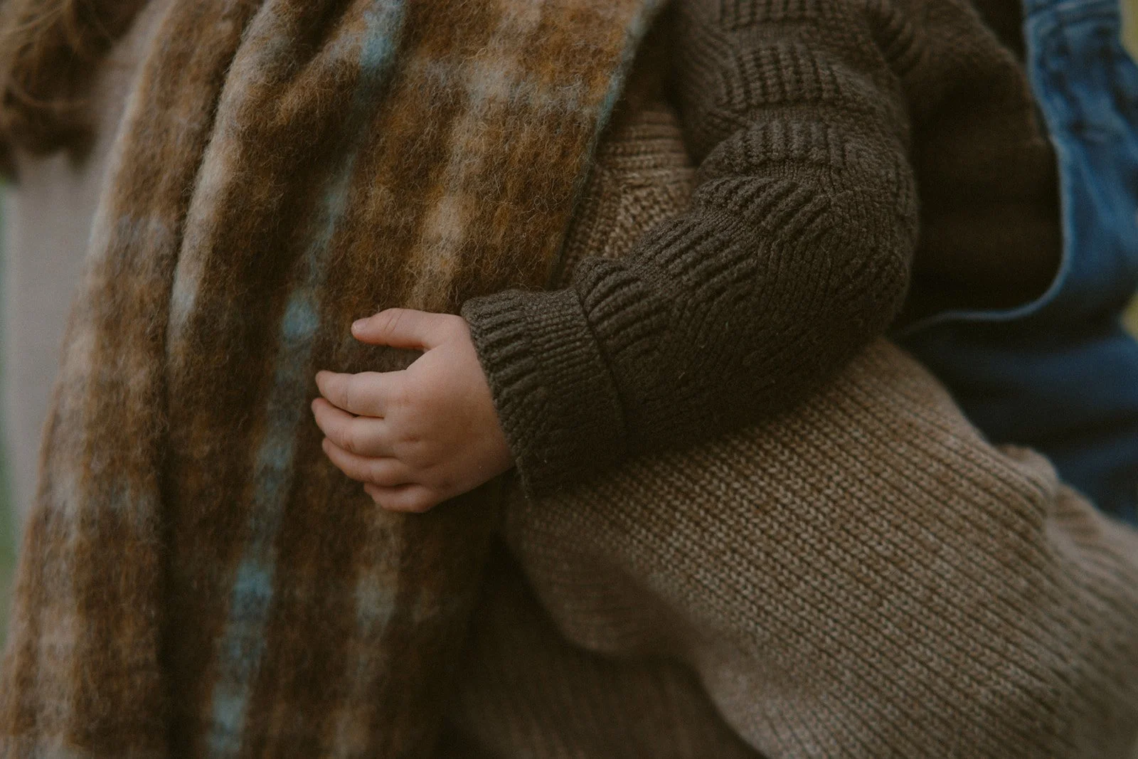 Close-up of a young child's hand grasping an adult's coat, both dressed in warm, textured clothing.