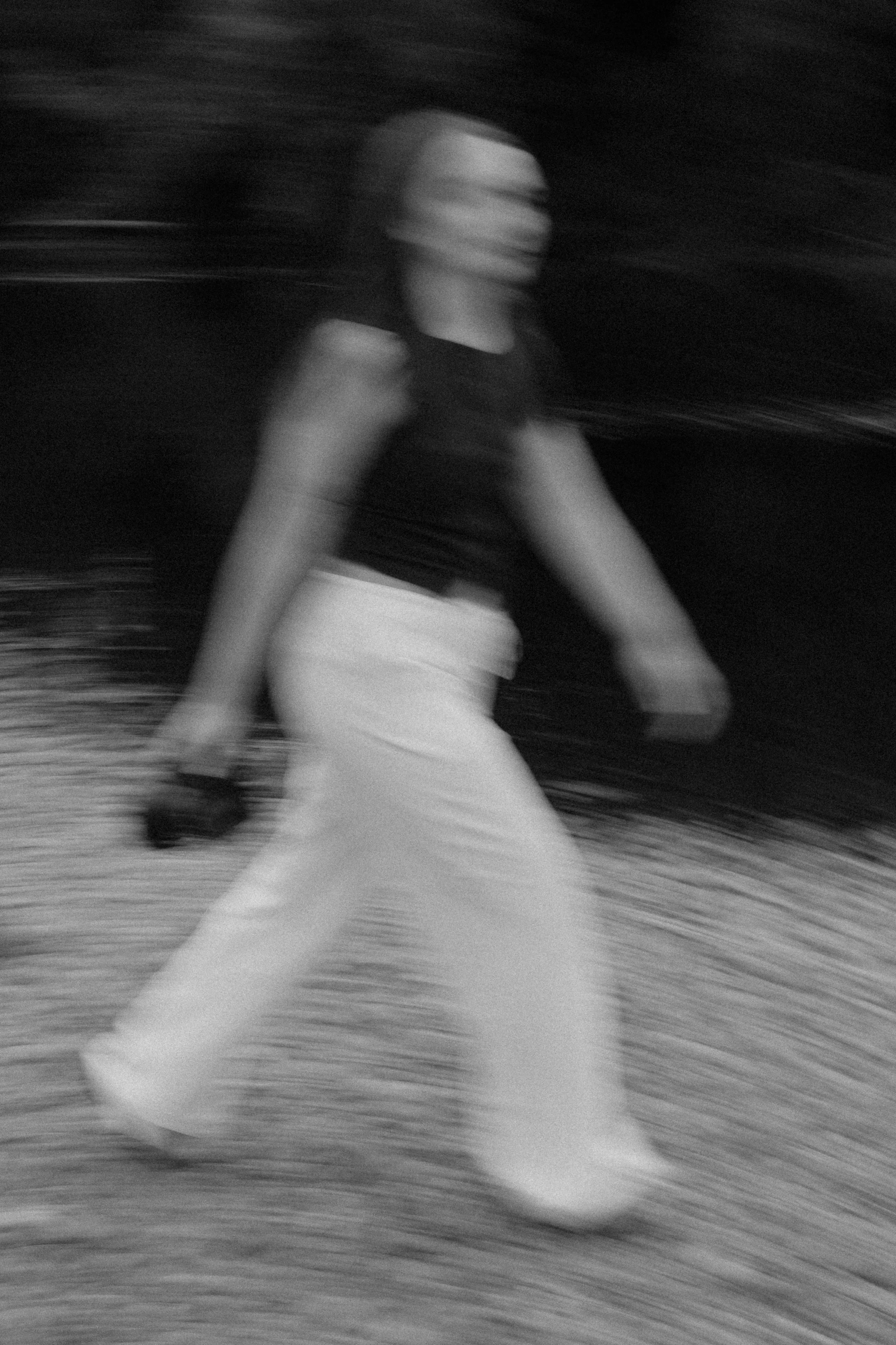 A woman walking outdoors at night, captured with motion blur, in black and white.
