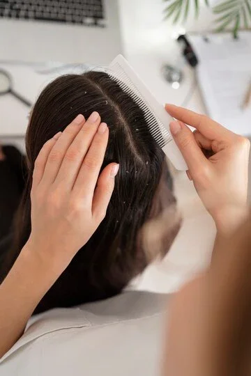 Person combing dark hair on a person's head in a hair salon.