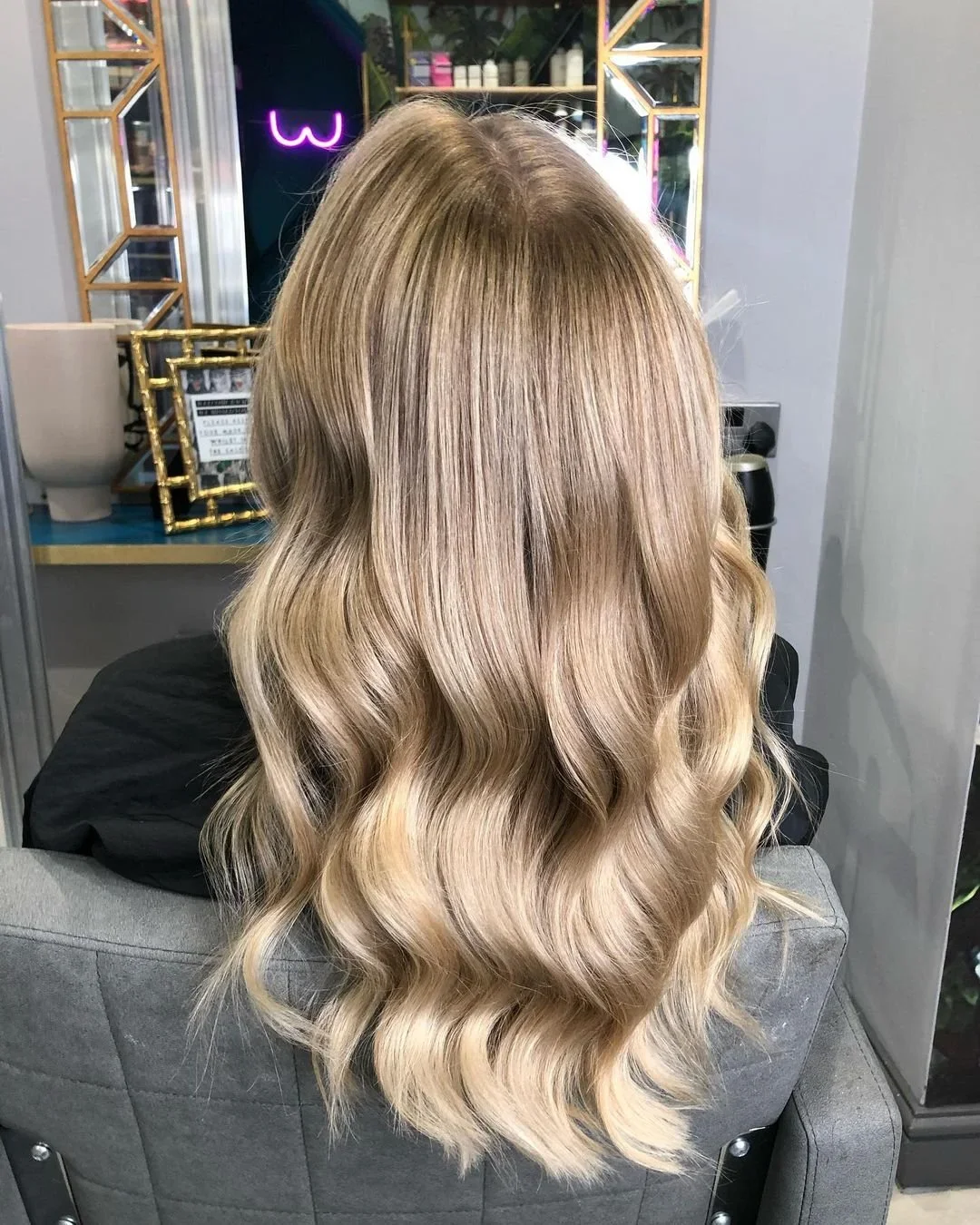 Back view of a woman with long, wavy blonde hair in a salon.