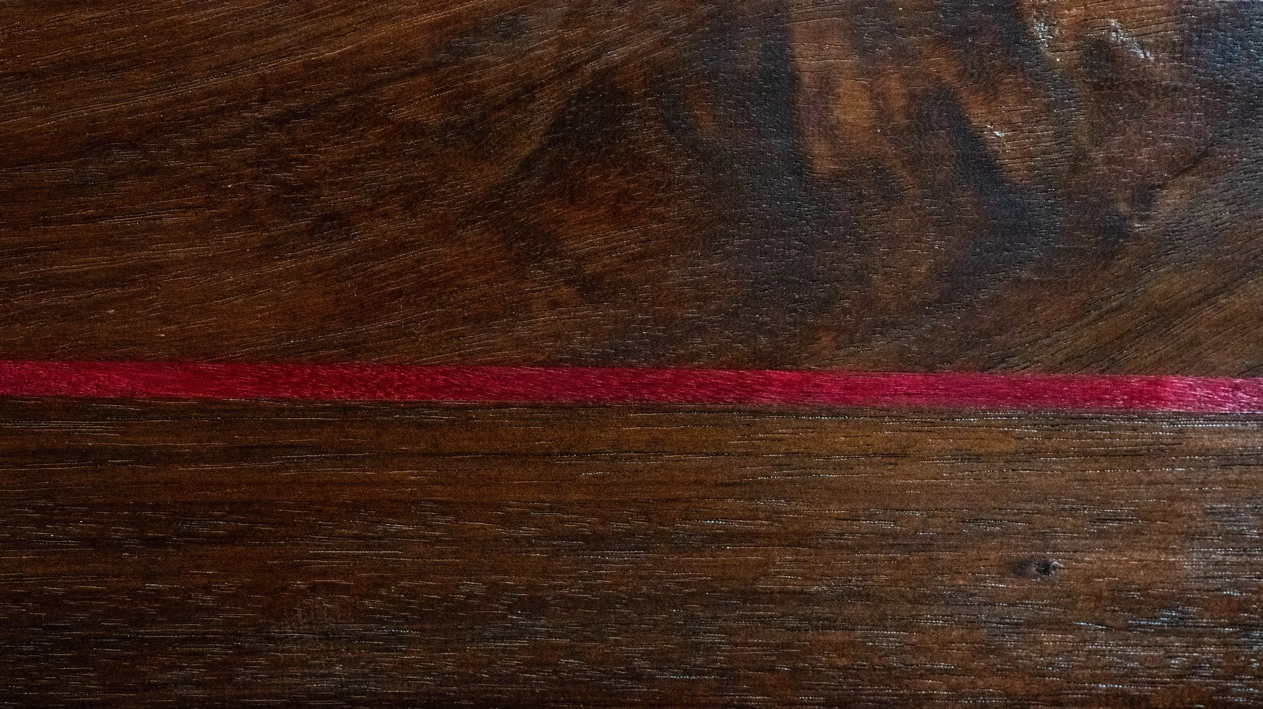 A close-up of a dark wooden surface with a red streak running across it.