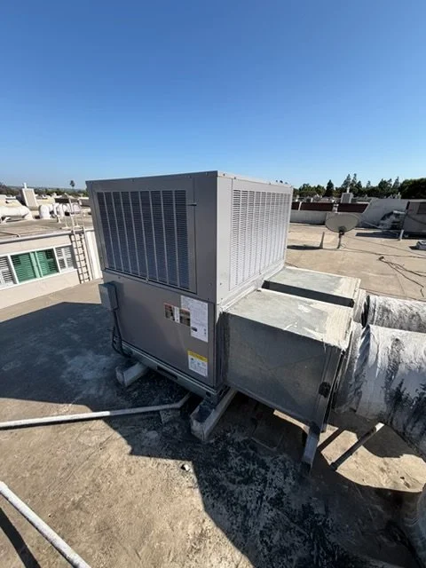 HVAC unit and duct system on a building rooftop under a clear blue sky.