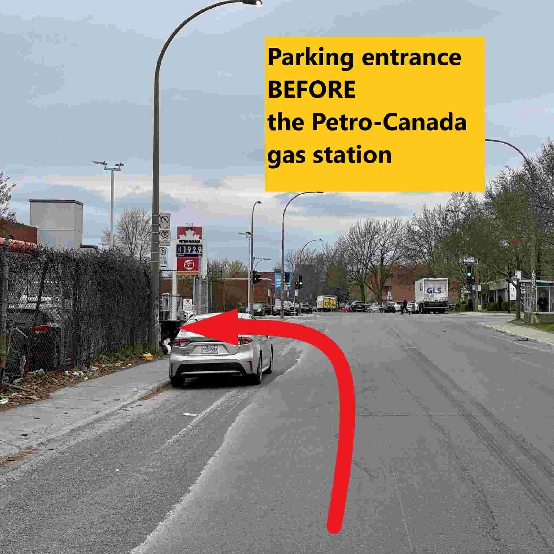Panneau jaune indiquant l'entrée du parking avant la station-service Petro-Canada, vue d'une rue avec des véhicules, des arbres et des lampadaires.