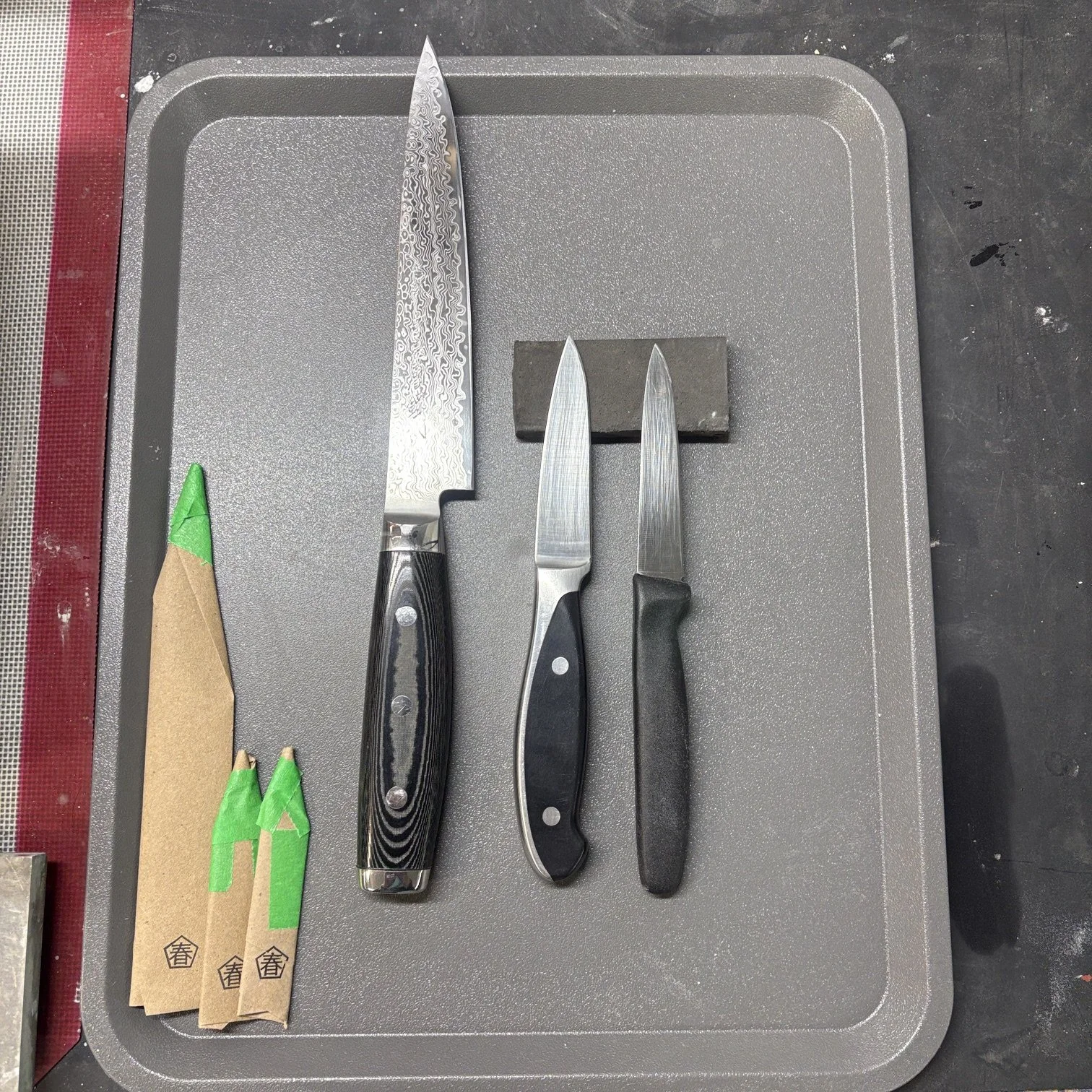 Trois couteaux de cuisine et deux paquets de baguettes en bois. Les couteaux sont placés sur un plateau gris en plastique.