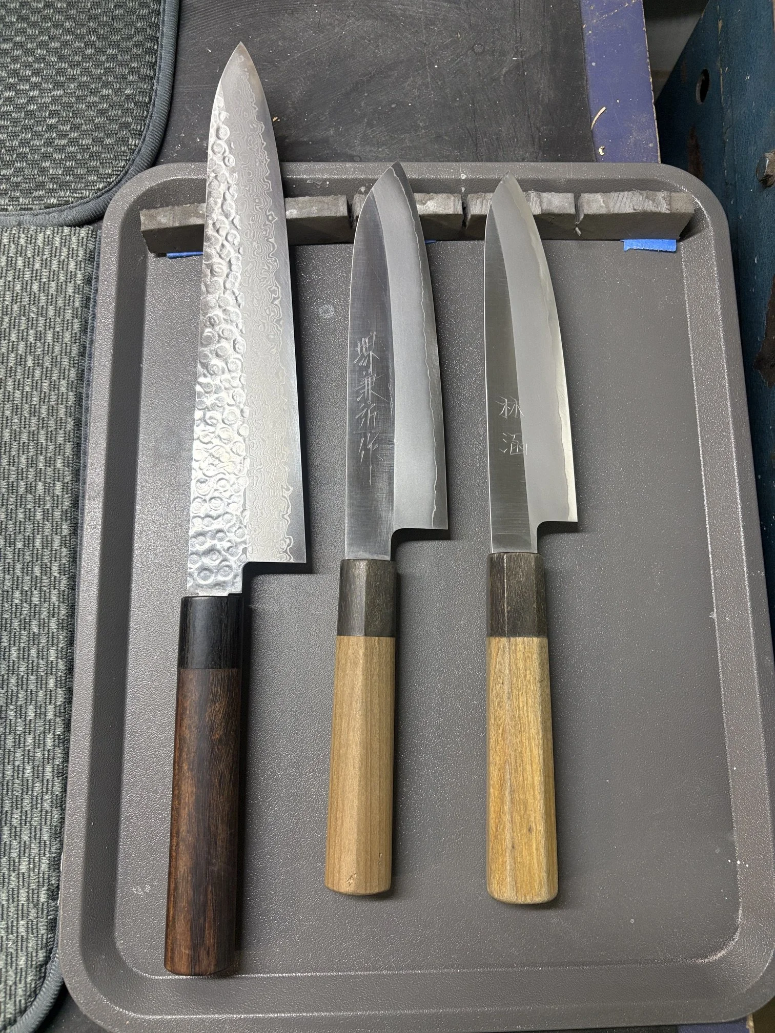 Quatre couteaux de cuisine avec manches en bois disposés sur un plateau en plastique gris.