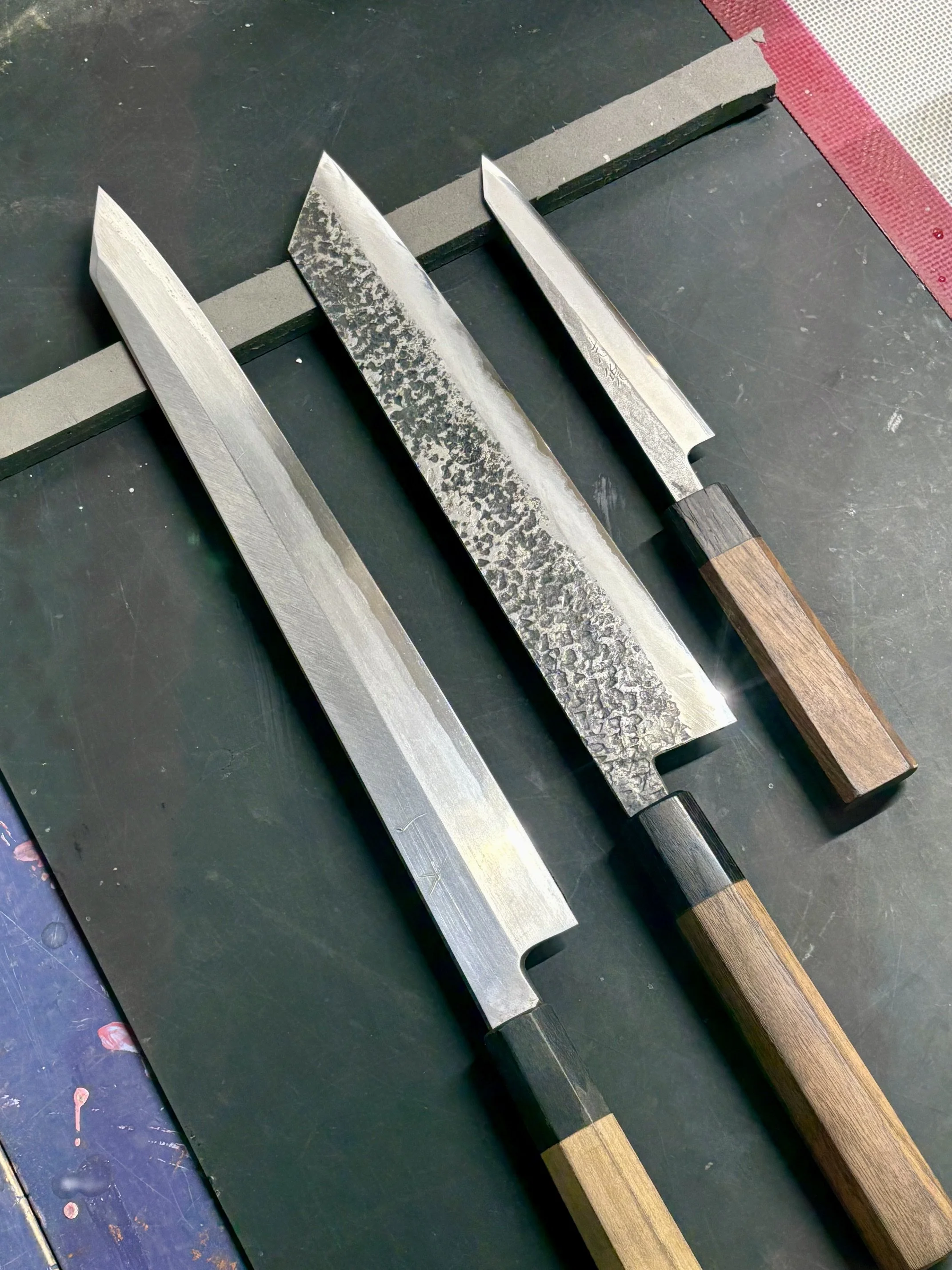 Trois couteaux avec manches en bois, posés sur une surface de travail noire.
