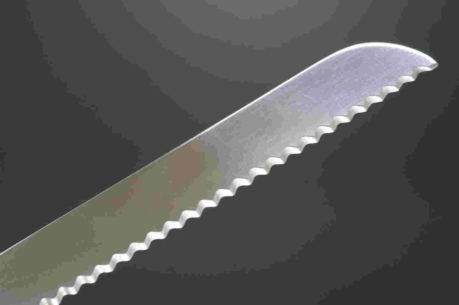 Un couteau de cuisine avec une lame en acier inoxydable brillant et une lame dentelée, posé sur un fond noir.