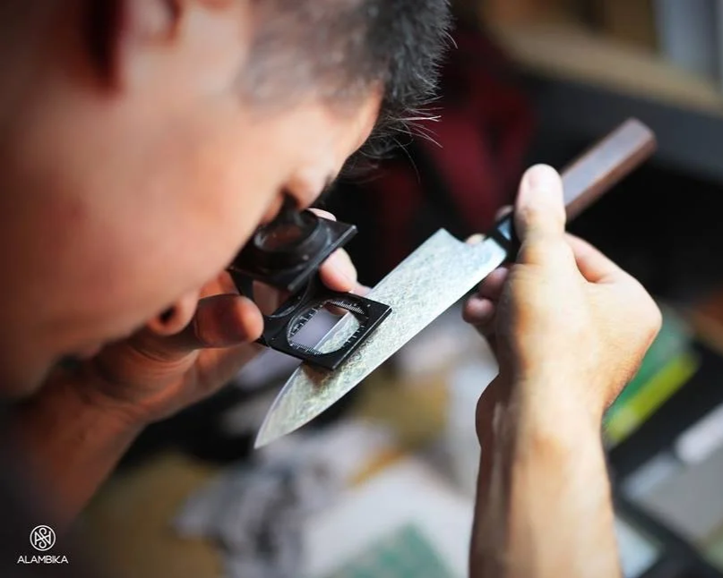 Une personne regarde à l'aide d'une une loupe la partie tranchante d'un couteau de cuisine.