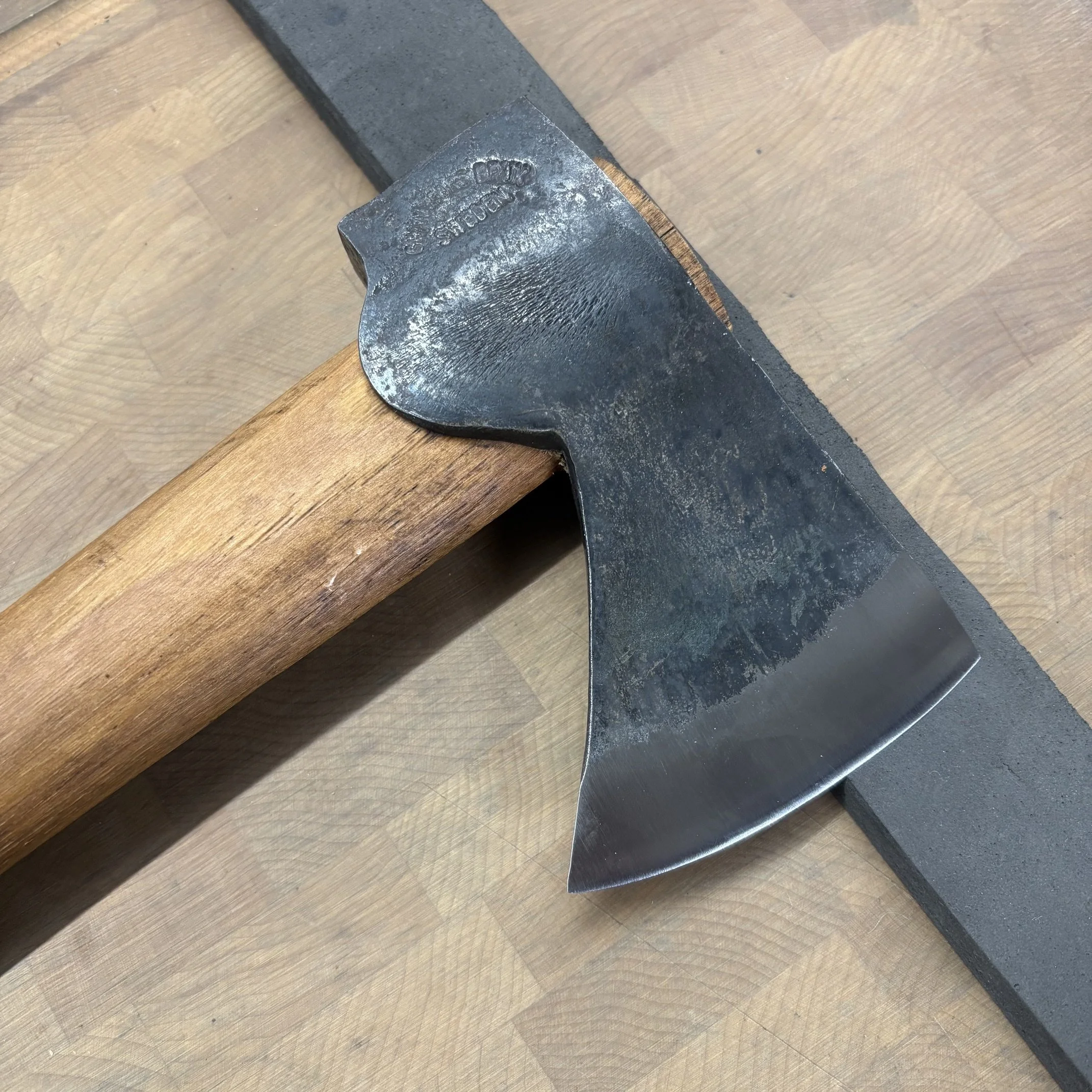 Une hache en acier posé sur une bande de mousse placé sur une planche en bois.