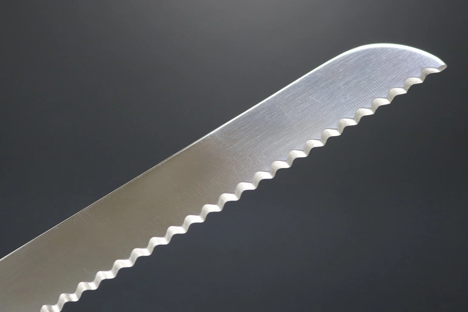 Une lame de couteau en acier inoxydable avec des dents dentelées, vue en gros plan contre un fond sombre.