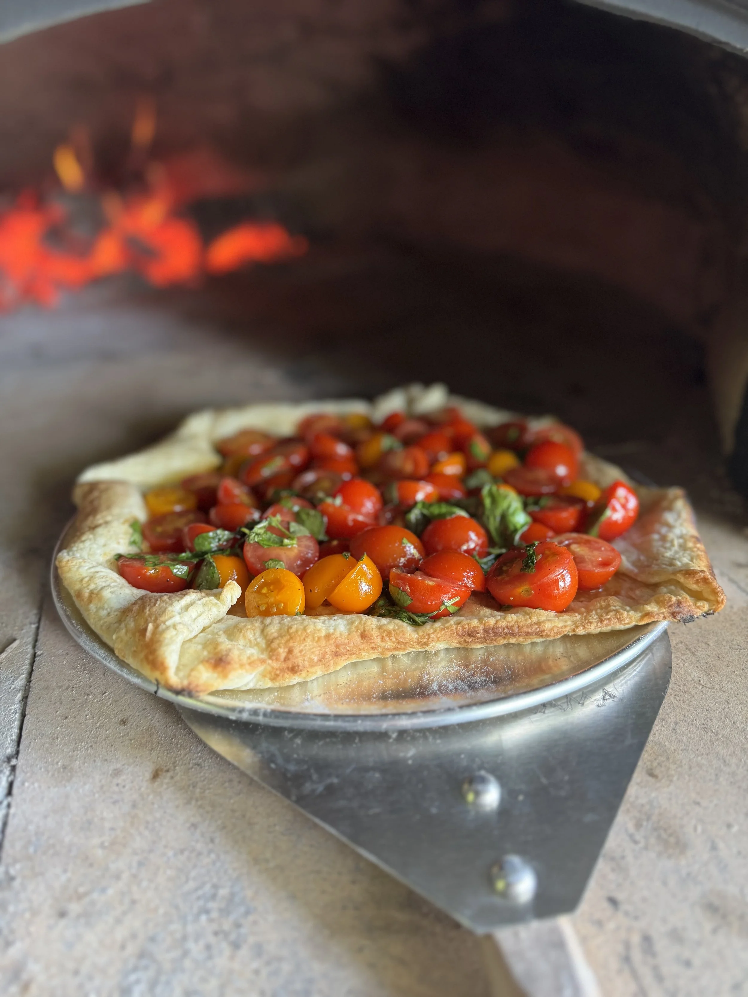 Pizza aux tomates cerises et basilic dans un four en pierre.
