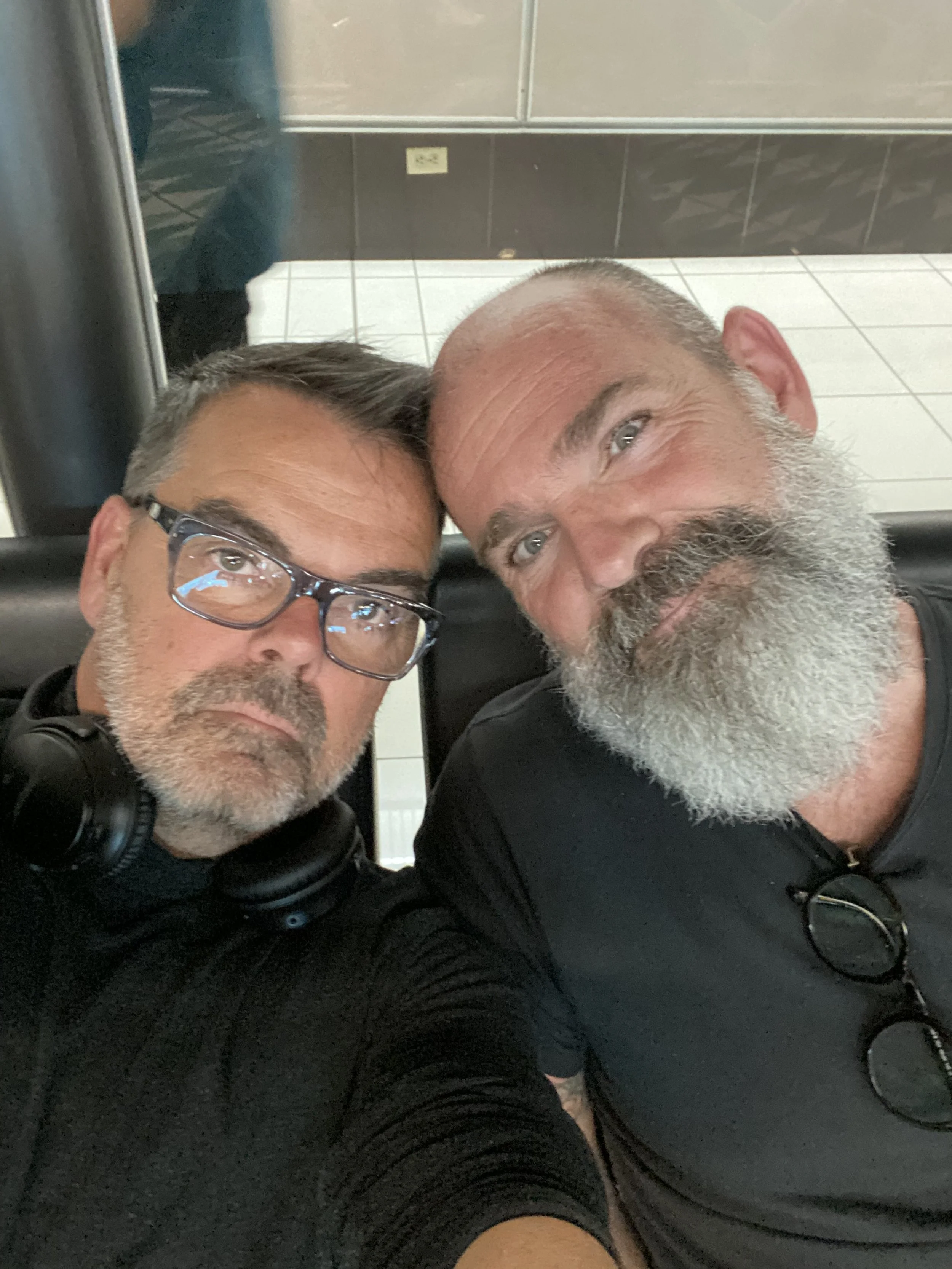 Deux hommes, propirétaire de la micro-ferme biologique "Les voisins & Cie", prennent une selfie ensemble. Ils sont assis contre un fond de mur et de miroir dans un lieu public.