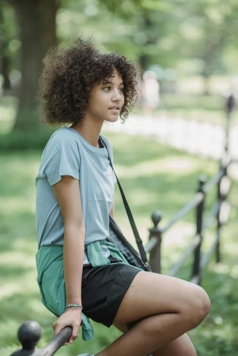 A teen girl sitting on a fence outside.