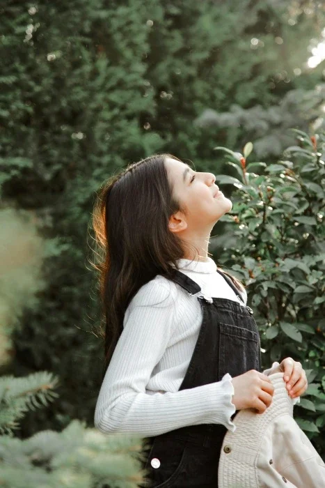 A teen girl wearing overalls, looking up to the sky.