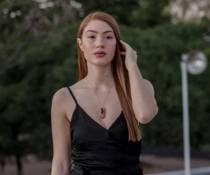 A woman outside, tucking her hair behind her ear.