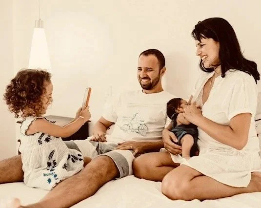 Family of four with two young children sitting on a bed and enjoying a joyful moment together.