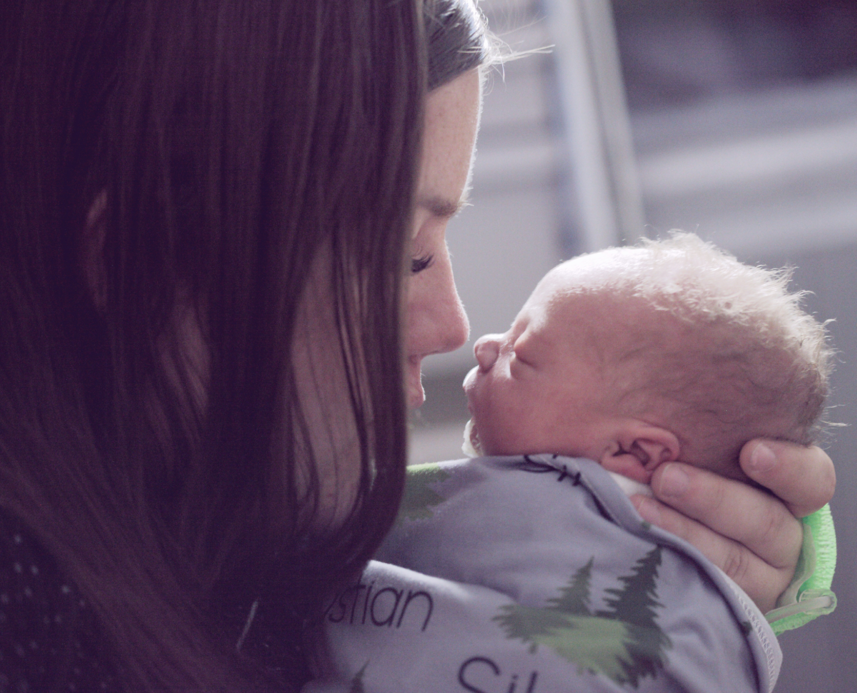 A woman with long dark hair holding a newborn baby face-to-face, both with eyes closed, in a tender moment.