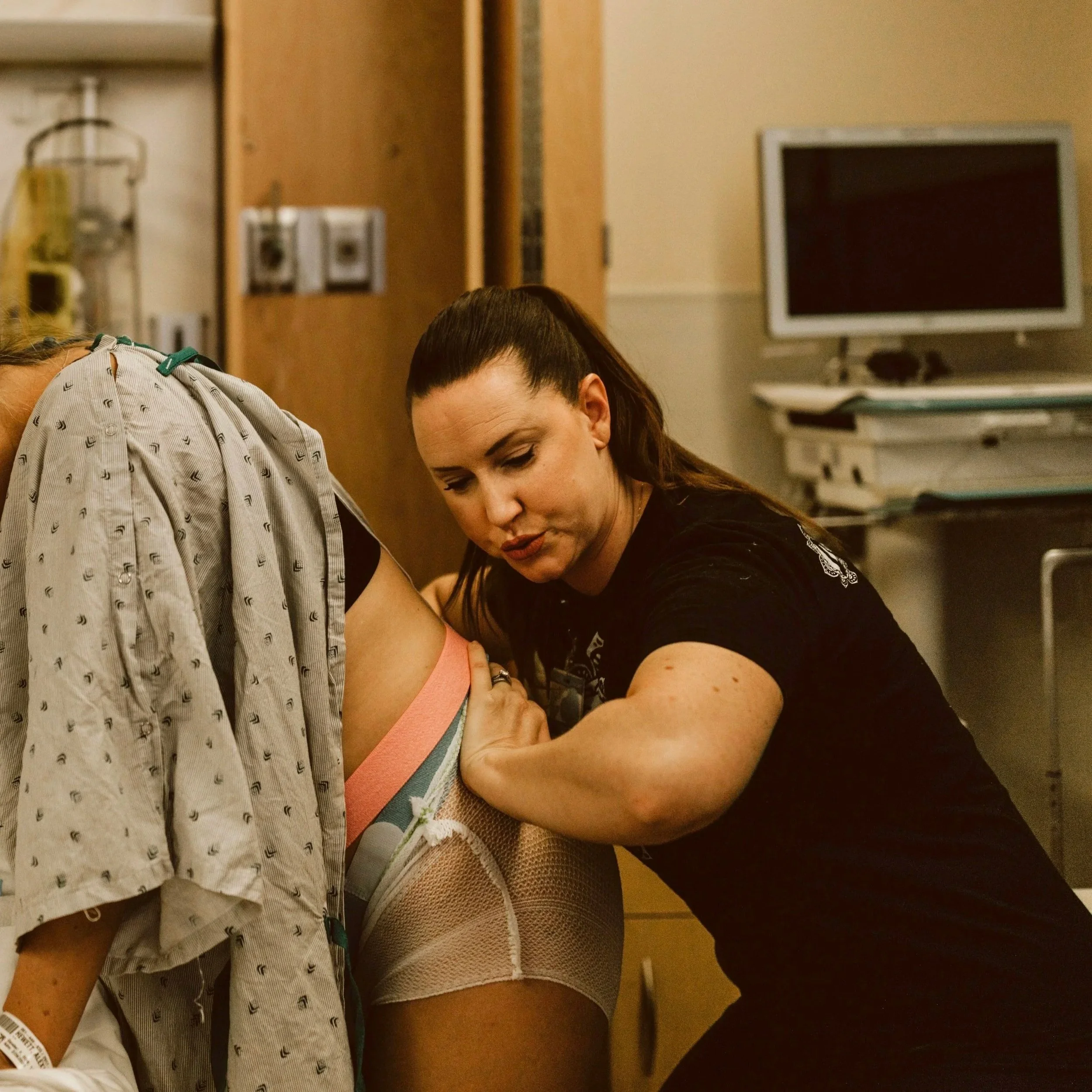 A doula or midwife applies counter pressure to the hips and back of a laboring women in a hospital room, touching the patient's side with her hand.