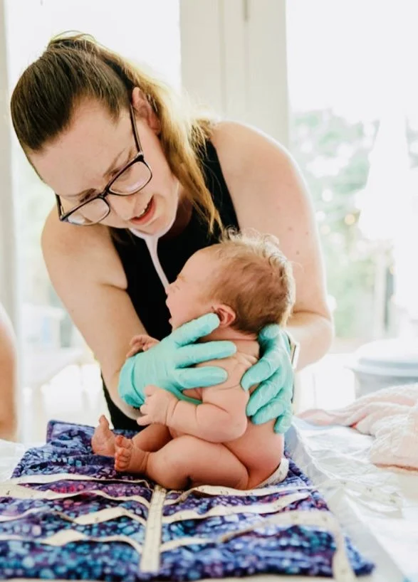 A licensed midwife holding a newborn baby performing a newborn exam at a home birth in Los Angeles. 