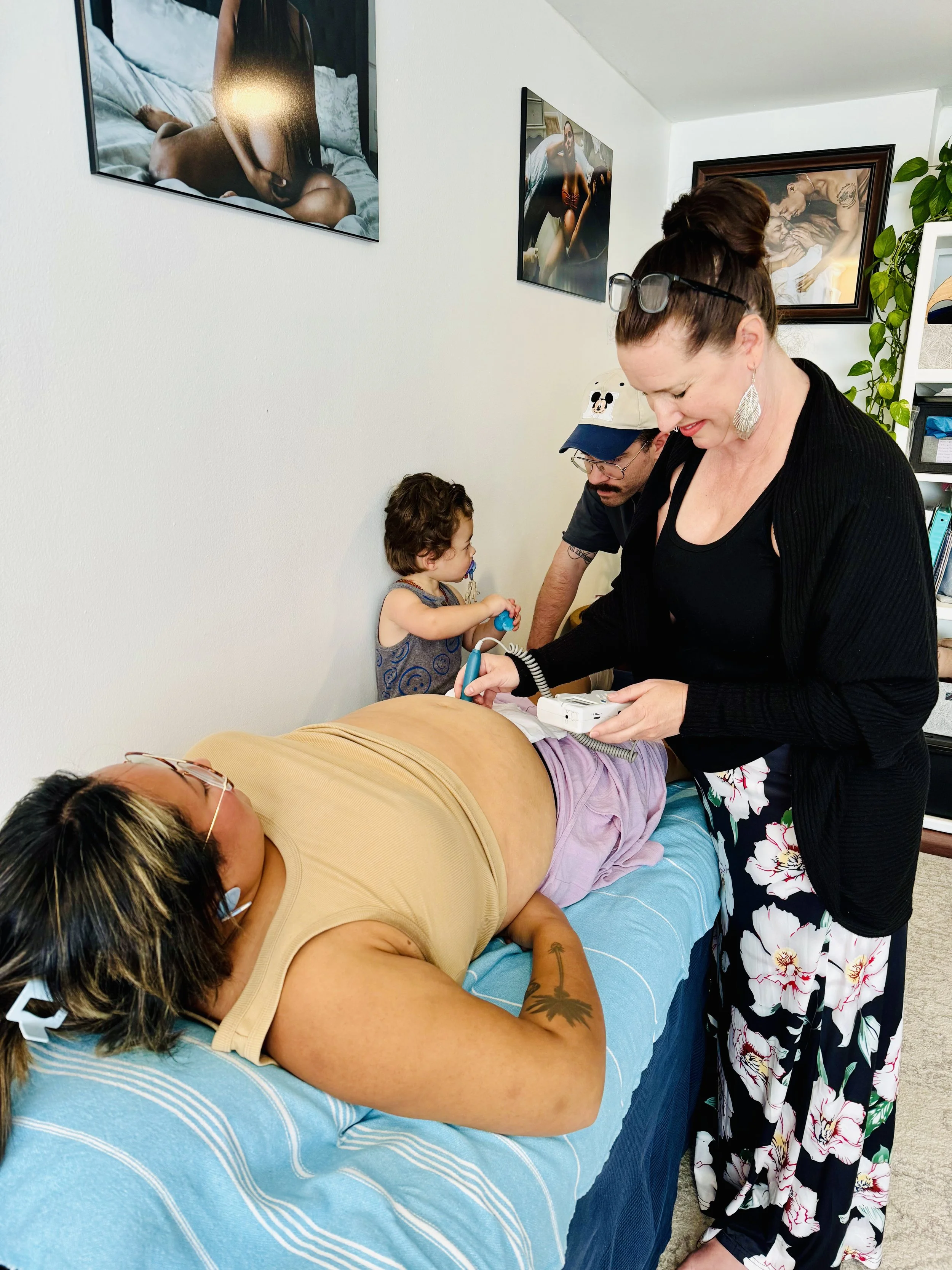 A pregnant woman is lying on an exam table while her midwife examines her. 