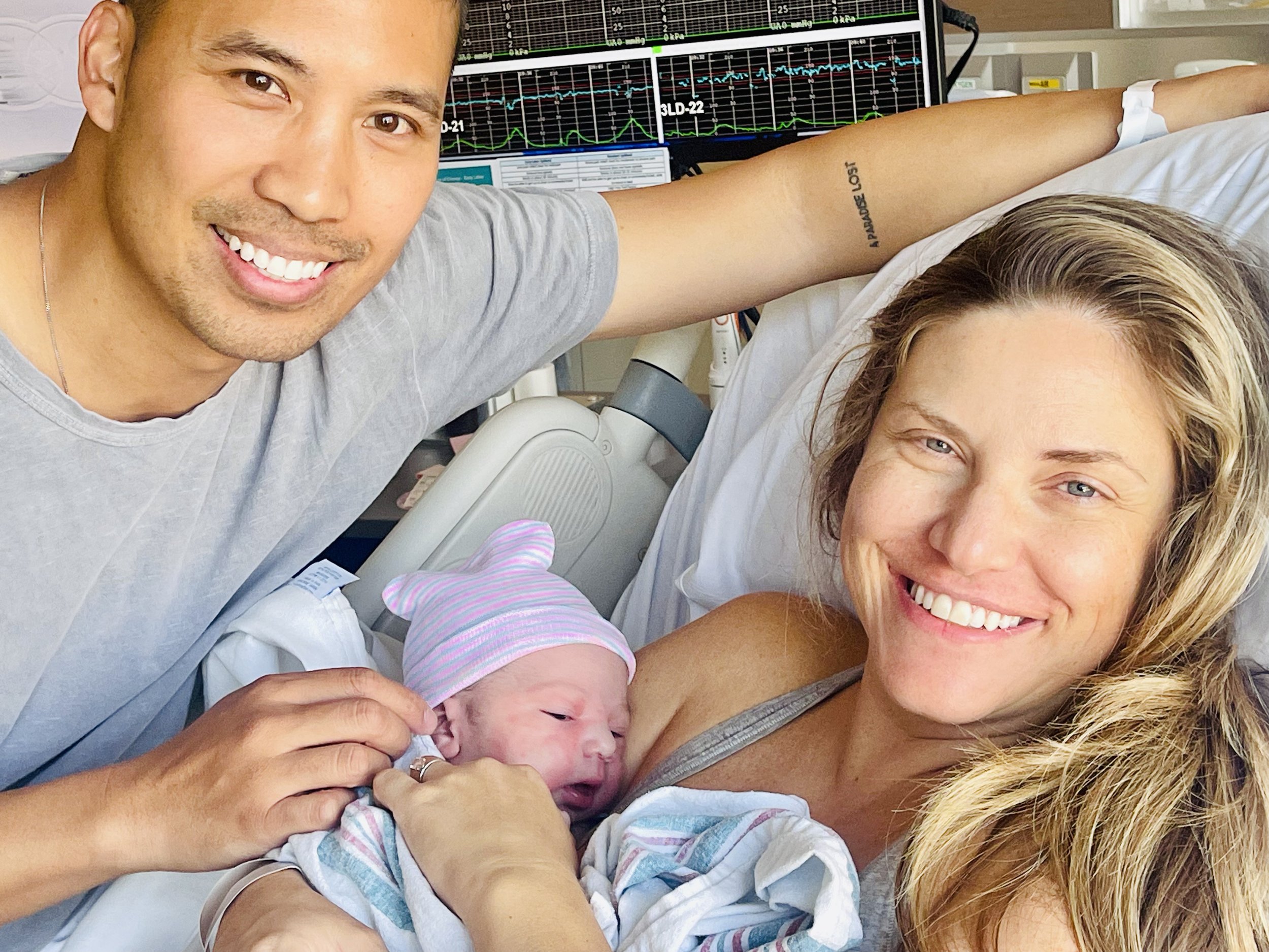 A couple holding a newborn in a hospital room with the support of a licensed midwife. 
