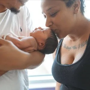 Woman gently touching kissing the head of her newborn baby's held by her partner.