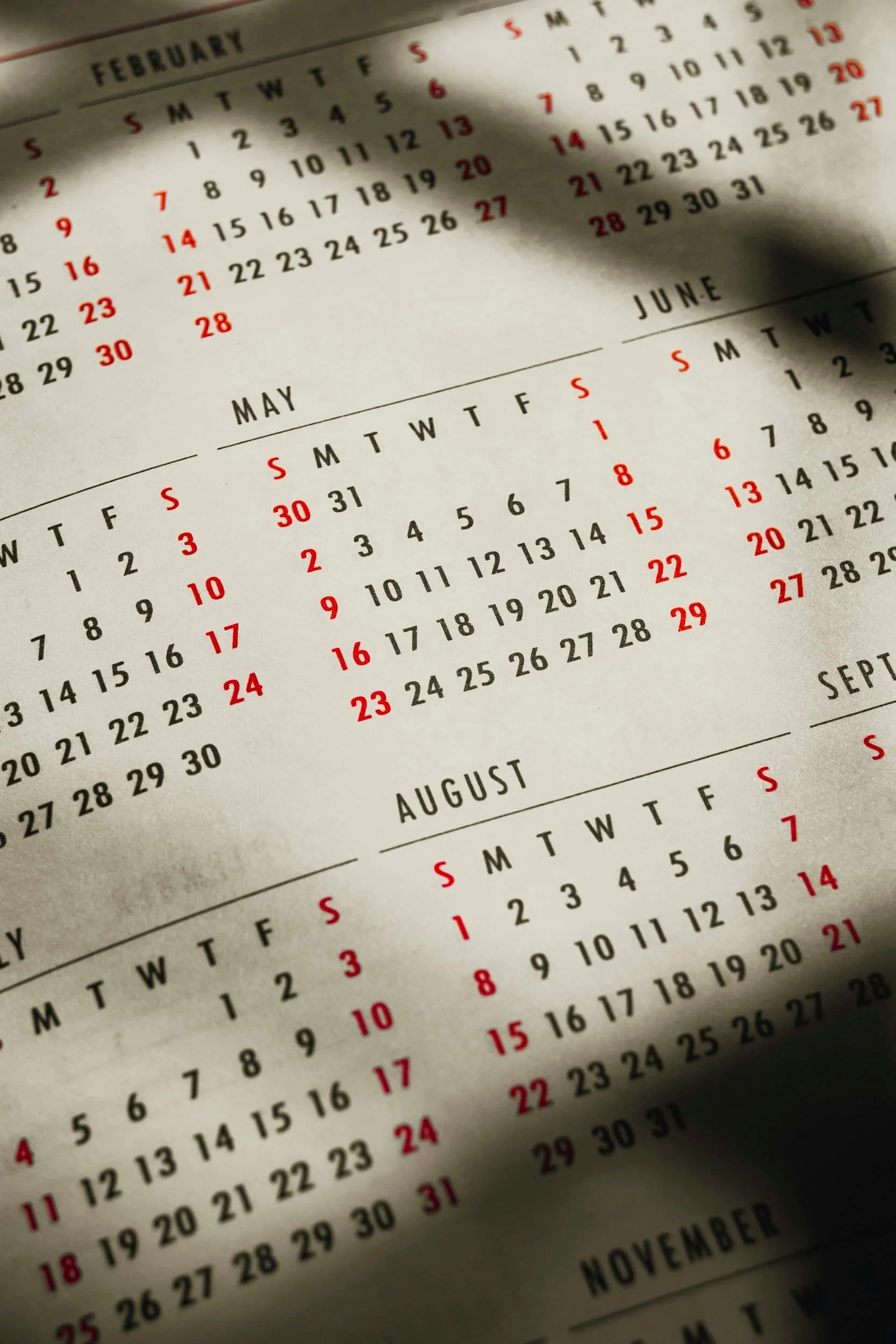 Close-up of a paper calendar showing February, May, June, August, and September months, with dates in black and Sundays marked in red.