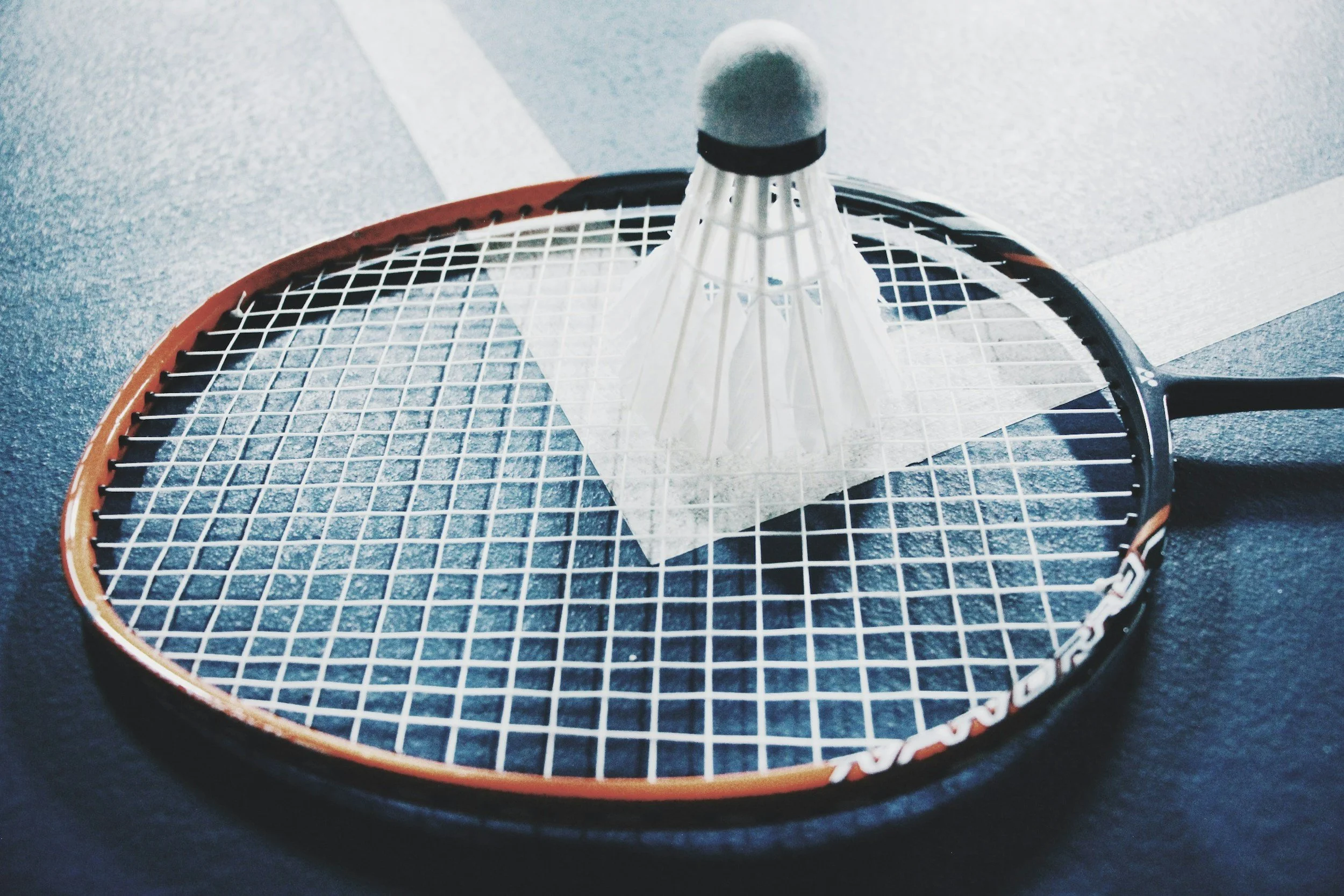 A tennis racket with a shuttlecock resting on its strings.