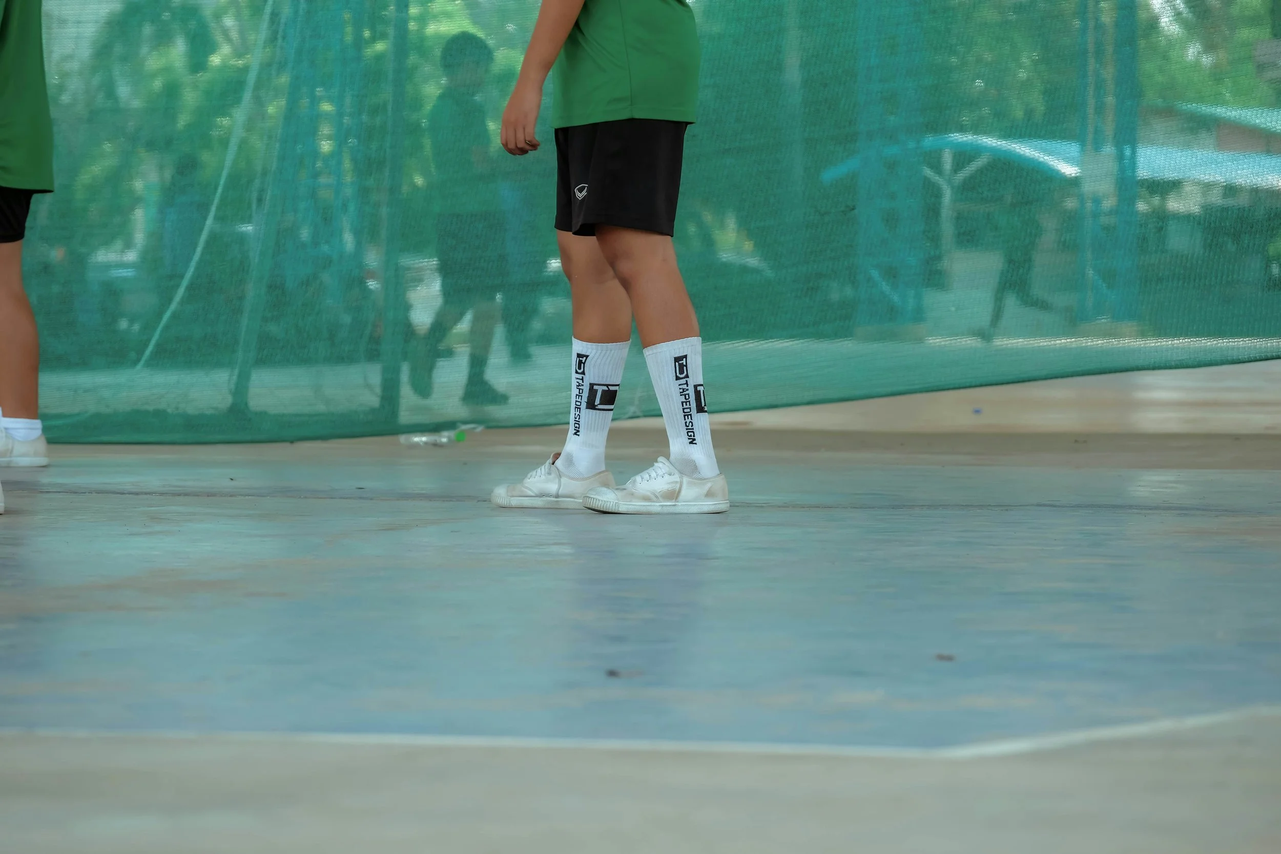 People in athletic clothing and white shoes standing behind a green barrier on a court.