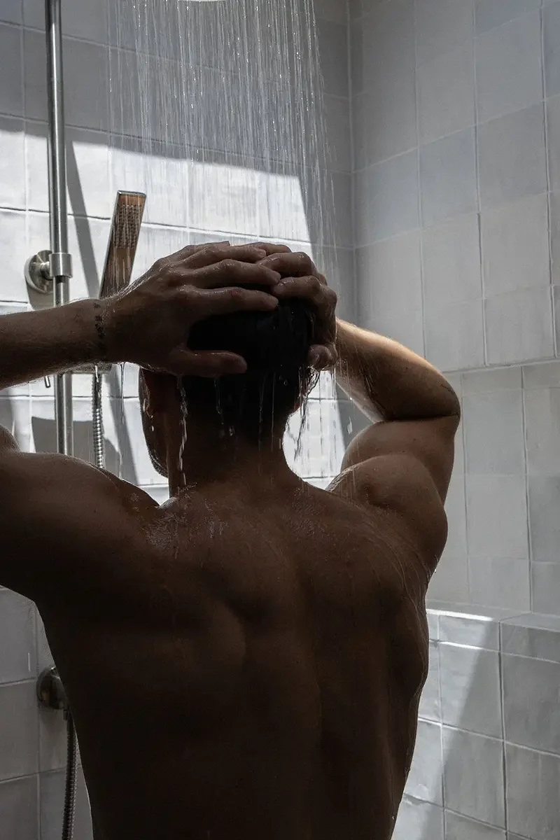 Person taking a shower, holding their head with both hands.