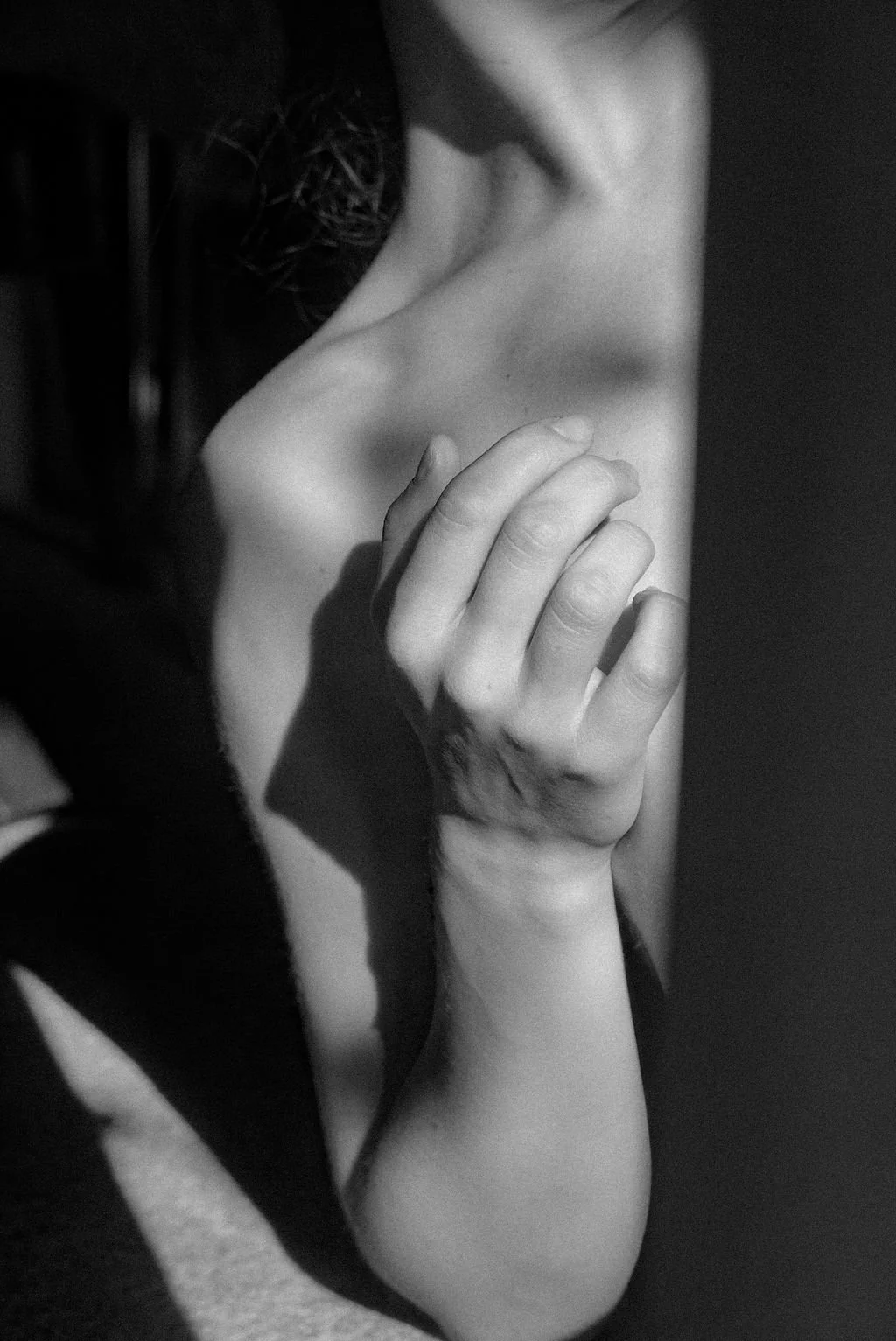 A close-up black and white photograph of a person's shoulder, hand, and part of their face with their hand out in front of their chest.