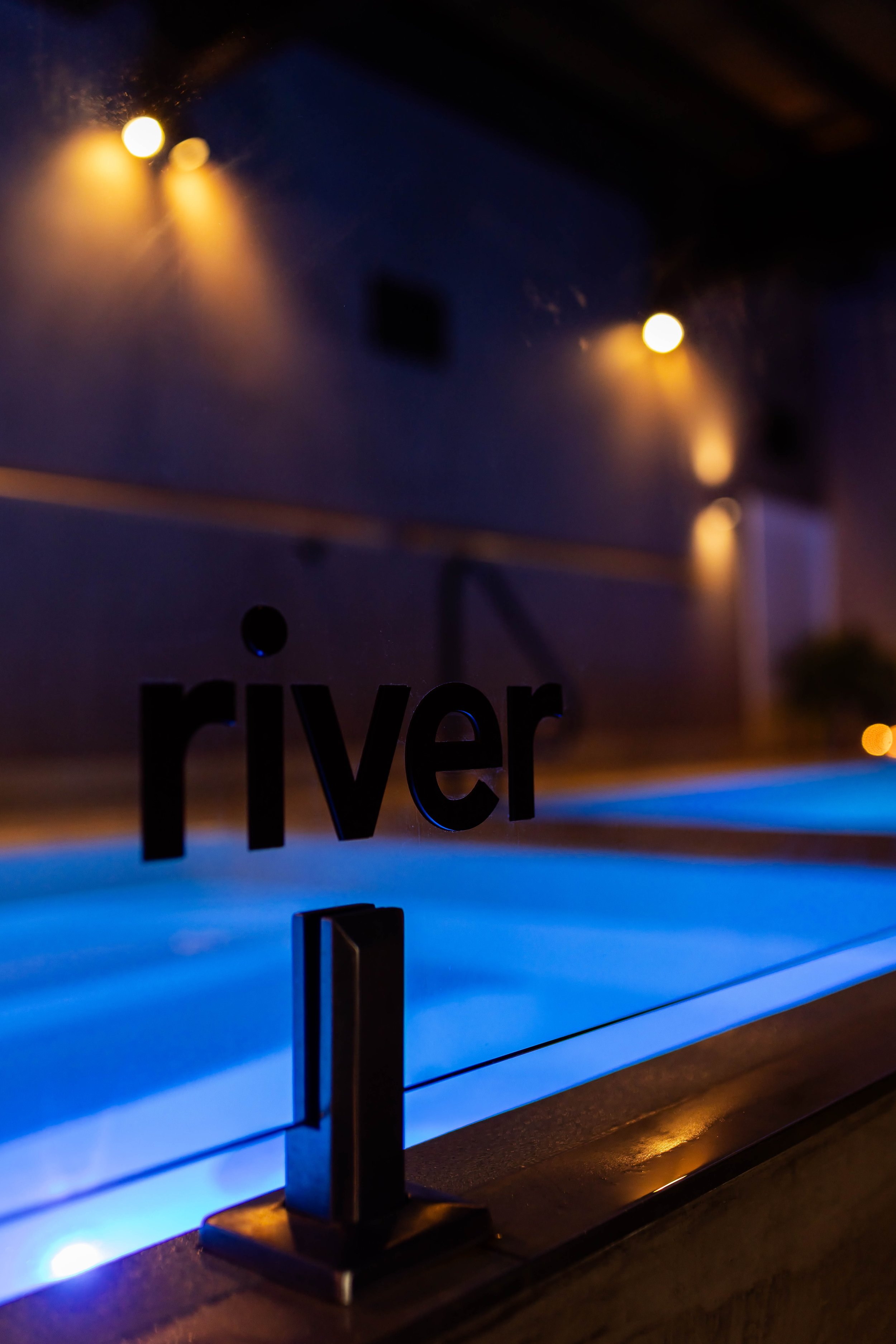 Close-up of a glass railing with the title 'river' describing the temperature of the pool.