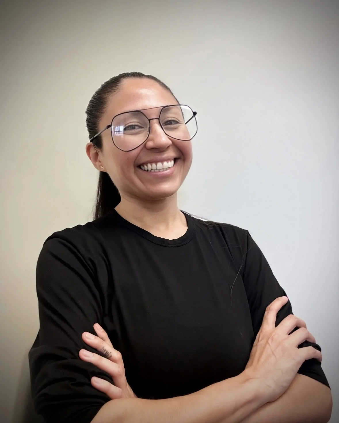 Woman with glasses and black long-sleeve shirt crossing her arms, smiling confidently and warmly at the camera